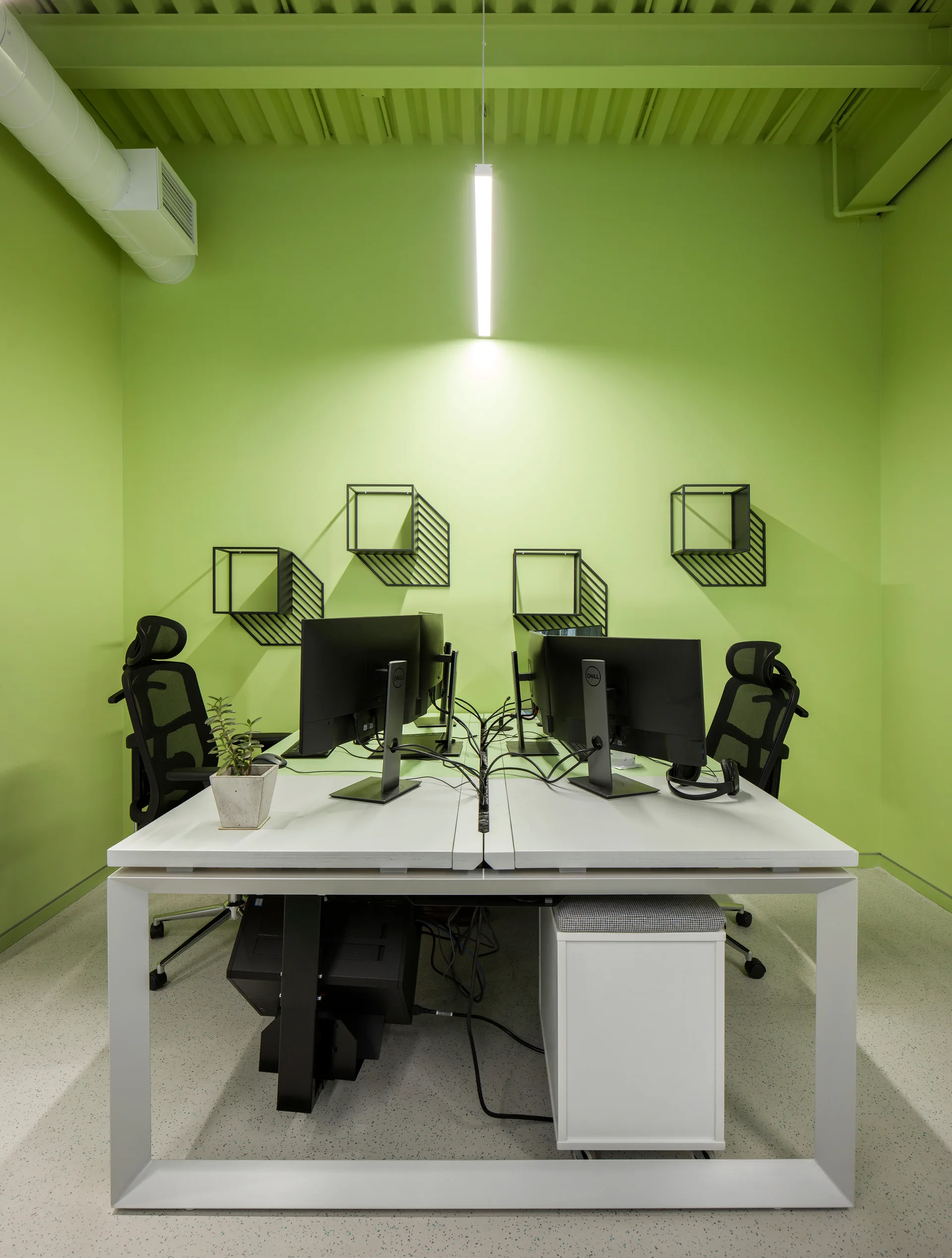 A minimalist white workstation with black monitors sits in a room with lime green walls, black wire cube shelves, and a matching painted ceiling.