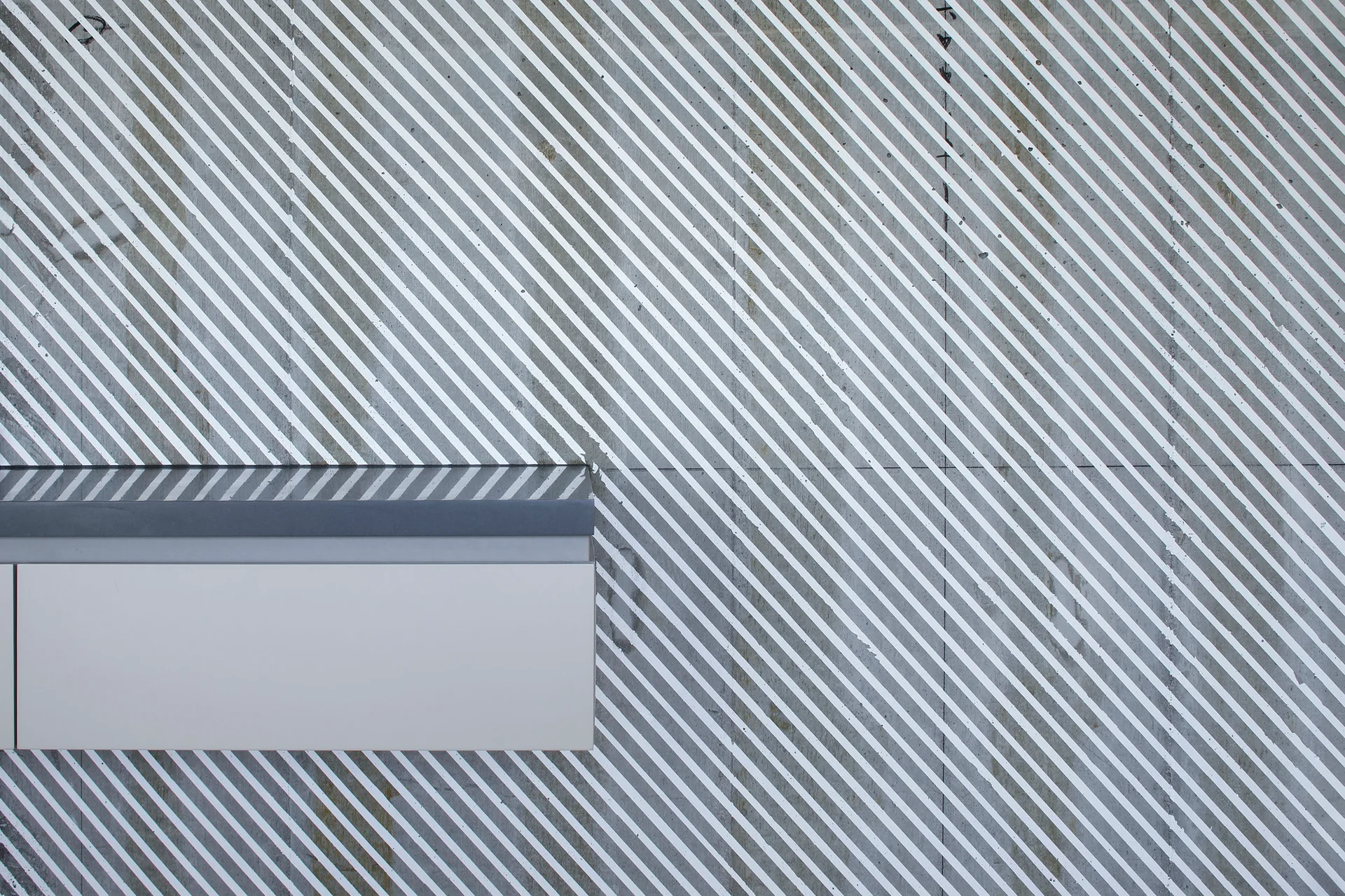 A close-up of a textured grey concrete wall featuring white diagonal stripes next to a minimalist grey and white cabinet edge.