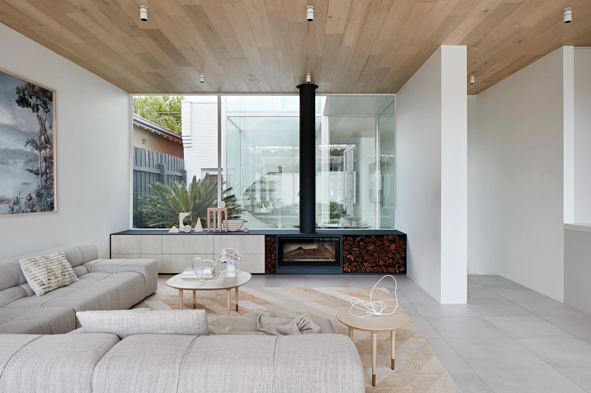 A modern living room featuring a grey modular sofa, a light wood plank ceiling, and a built-in media console with an integrated fireplace and log storage.