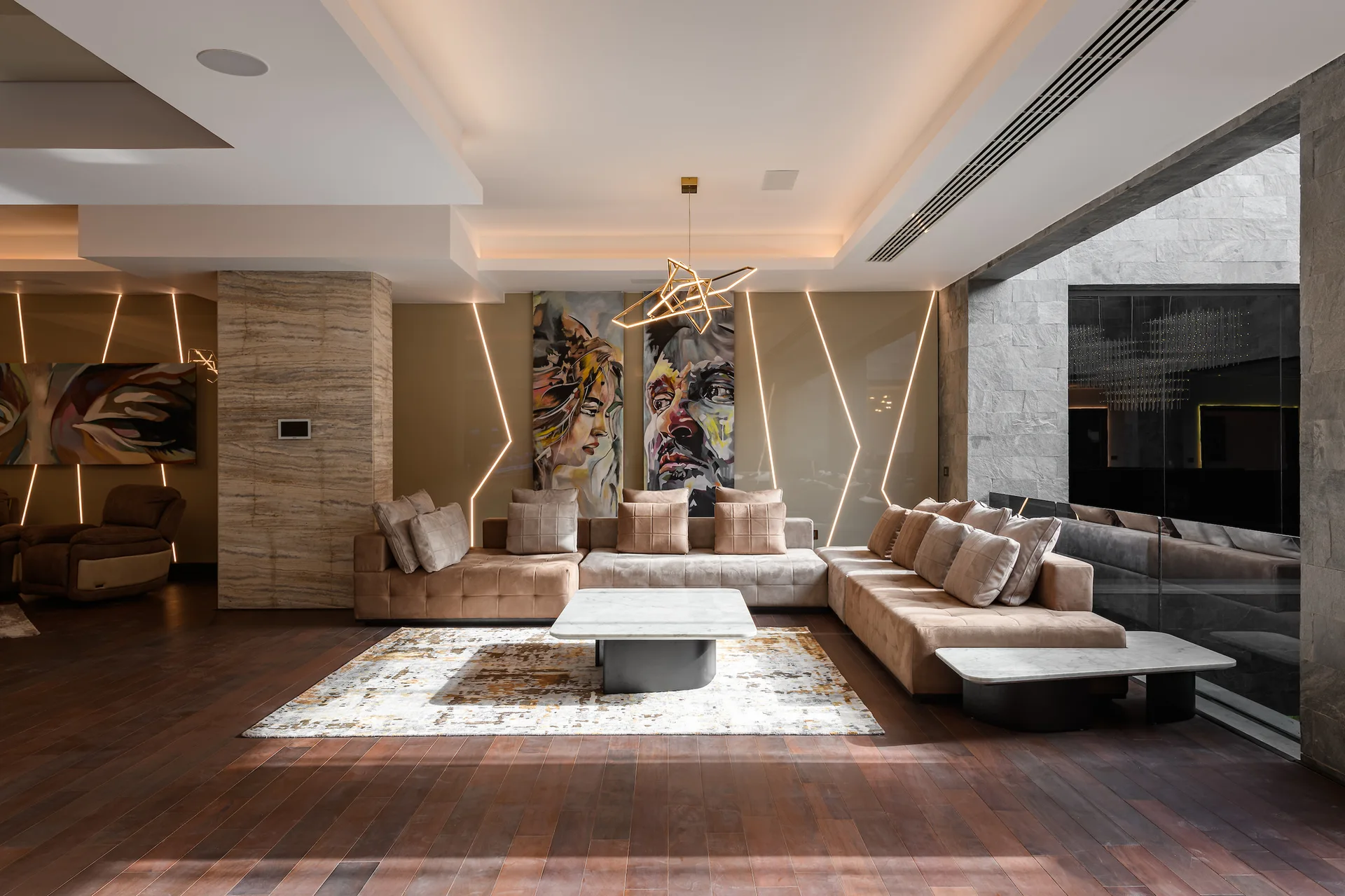 A spacious living room features a large modular beige sectional sofa, a marble-topped coffee table, and diagonal LED light strips embedded in the back wall.