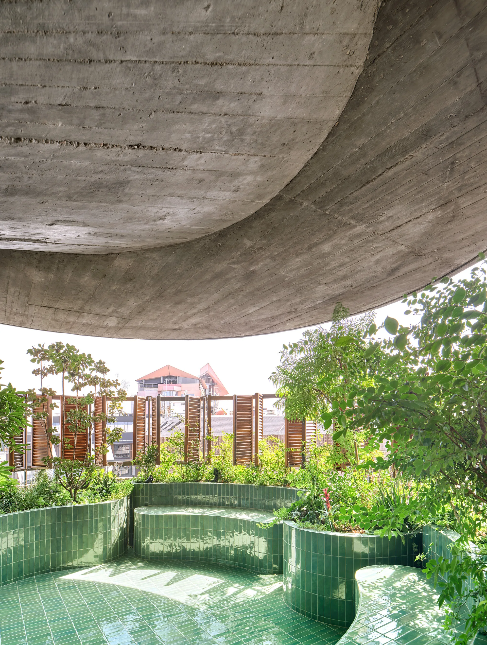 A rooftop terrace features a curved green tiled bench and integrated planters under a textured concrete ceiling with wood shutter screens.