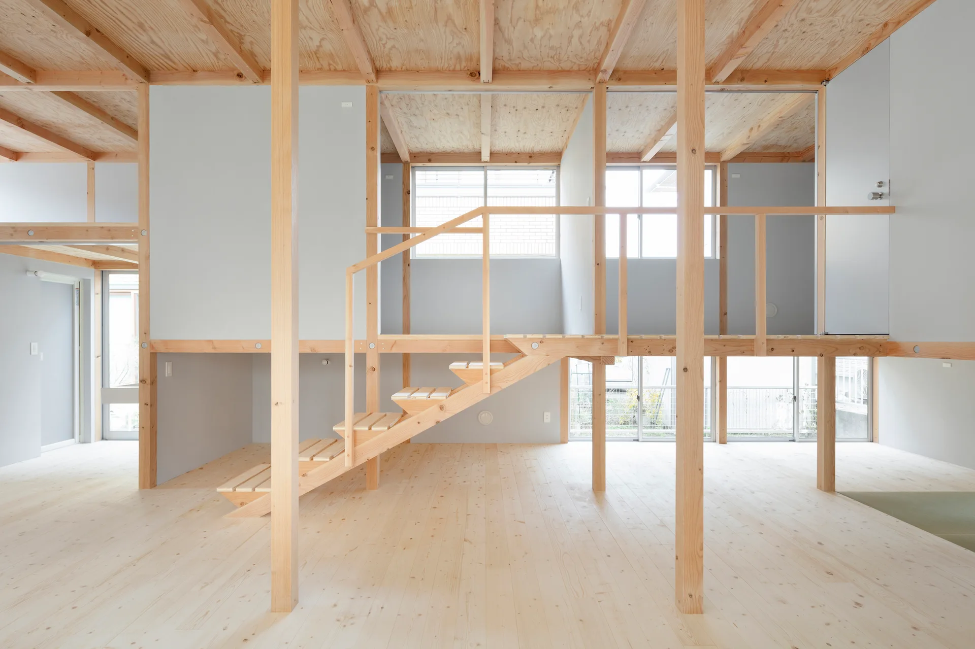 An open plan home interior featuring light wood structural posts, a central open tread staircase, and light grey walls.