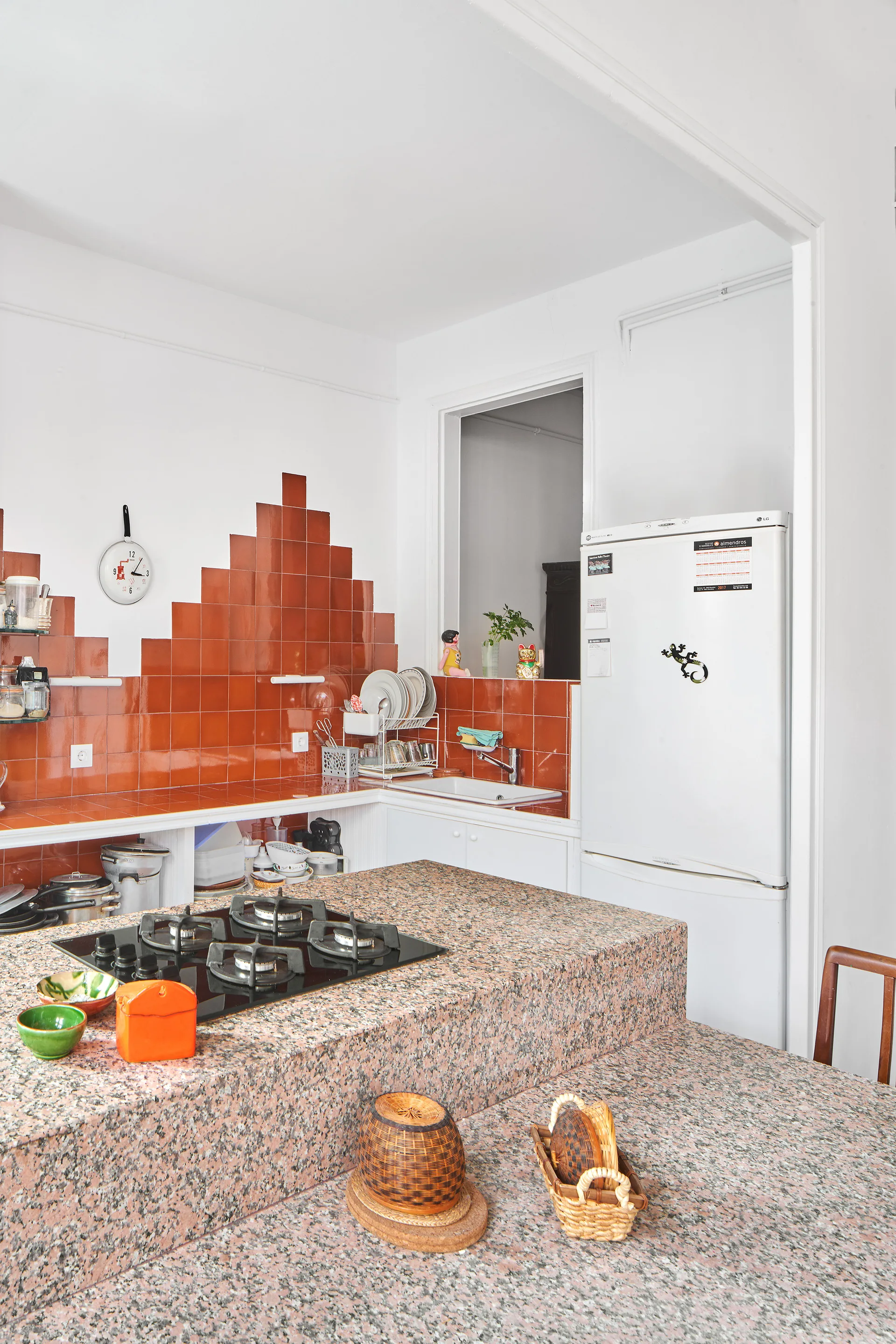 An eclectic kitchen featuring a pink speckled granite island with a built-in cooktop and a stepped terracotta tile backsplash.