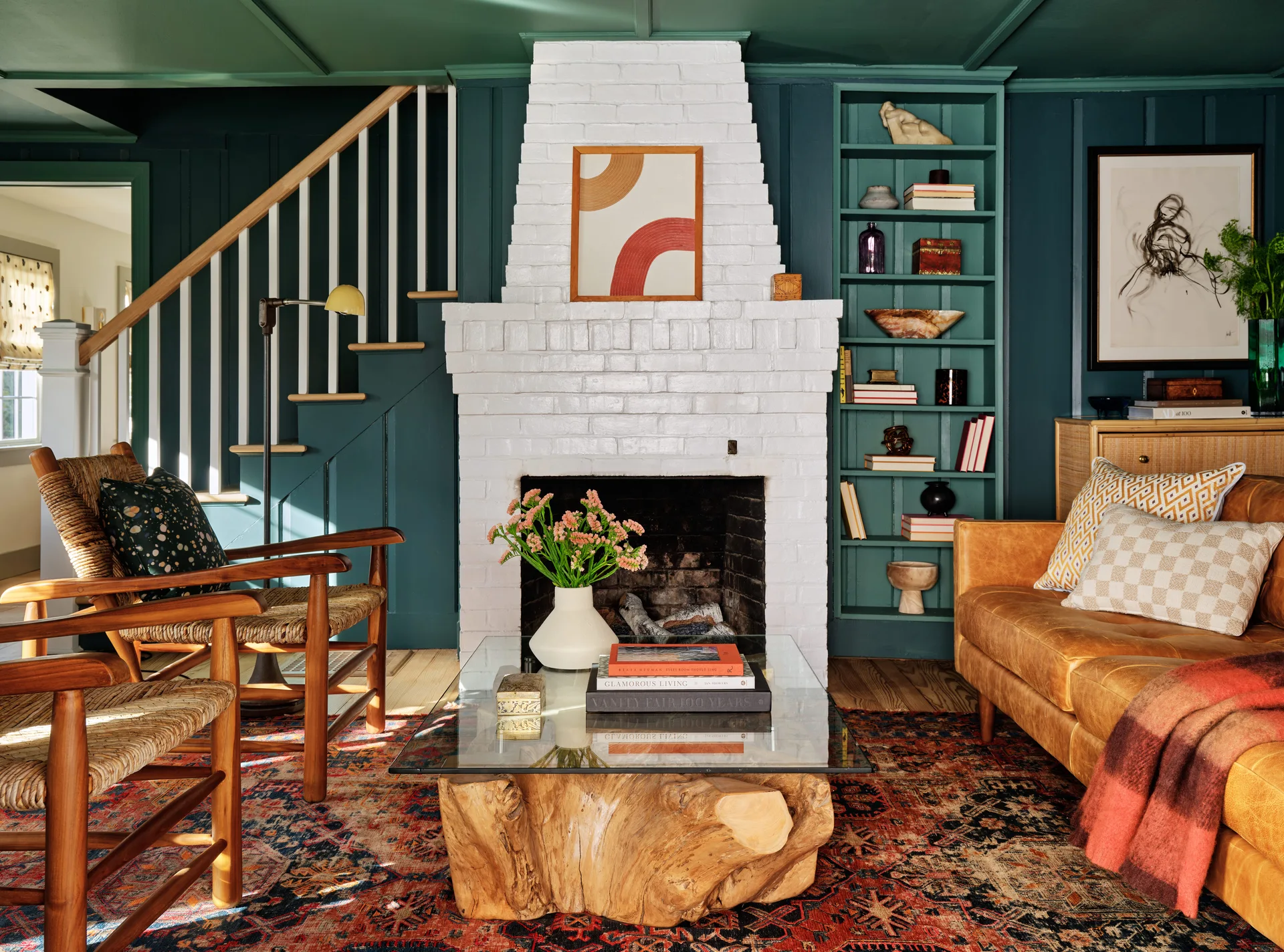 A teal-painted living room featuring a white brick fireplace, built-in shelving, a tan leather sofa, and wood armchairs on an oriental rug.