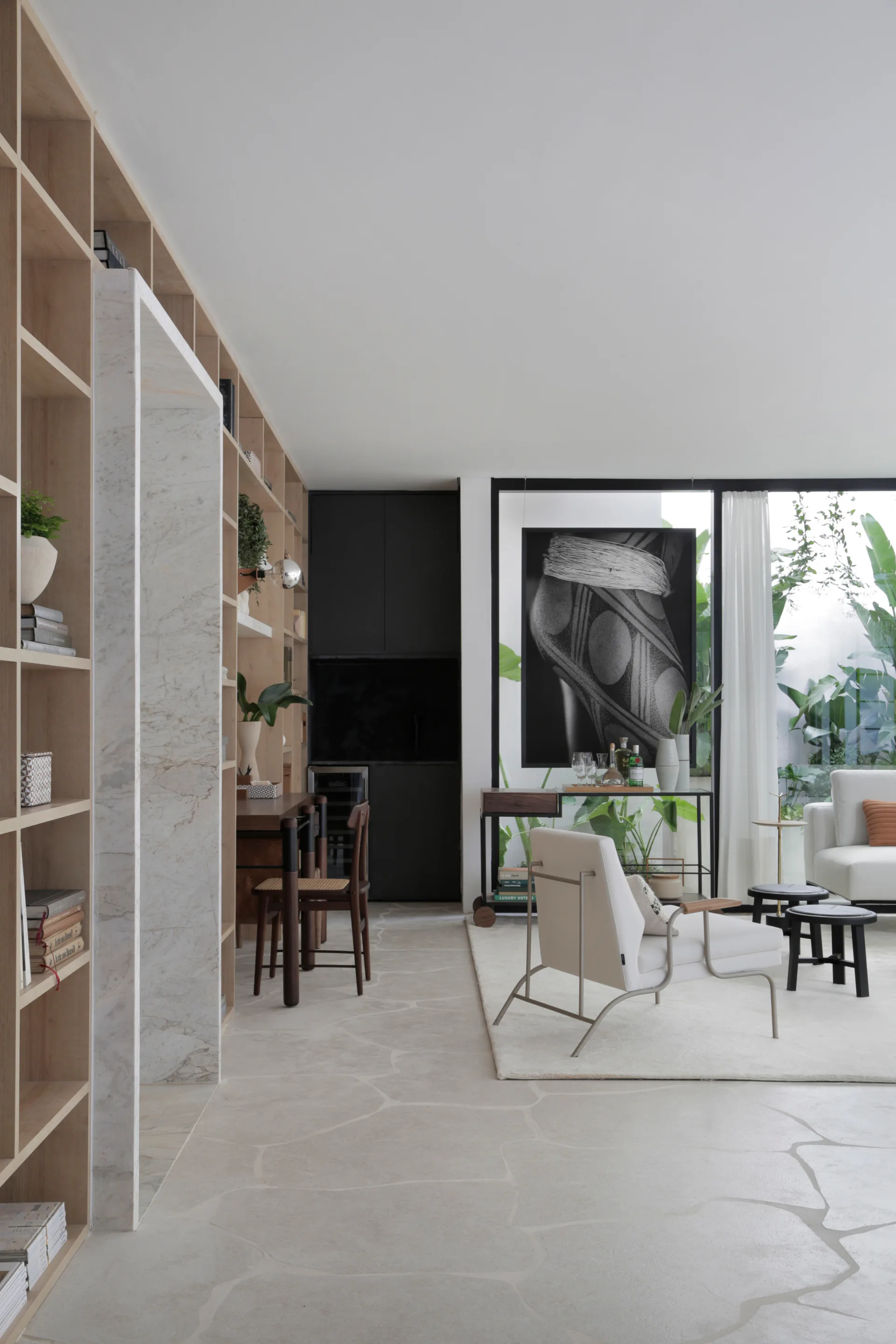 A contemporary living room features floor-to-ceiling wood bookshelves, a large marble portal, irregular flagstone tile floors, and a glass wall.