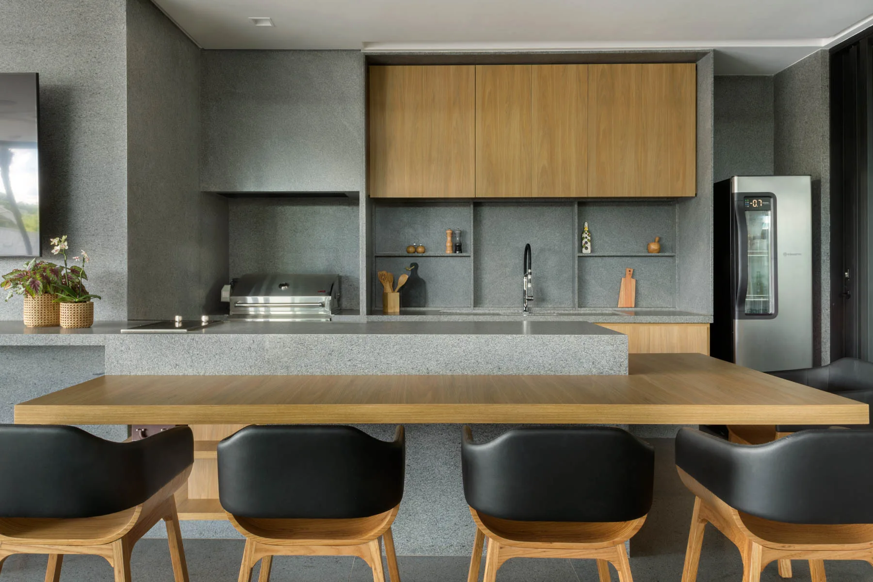 A modern kitchen featuring a textured grey stone wall, light wood upper cabinets, and a kitchen island with an attached wood breakfast table.