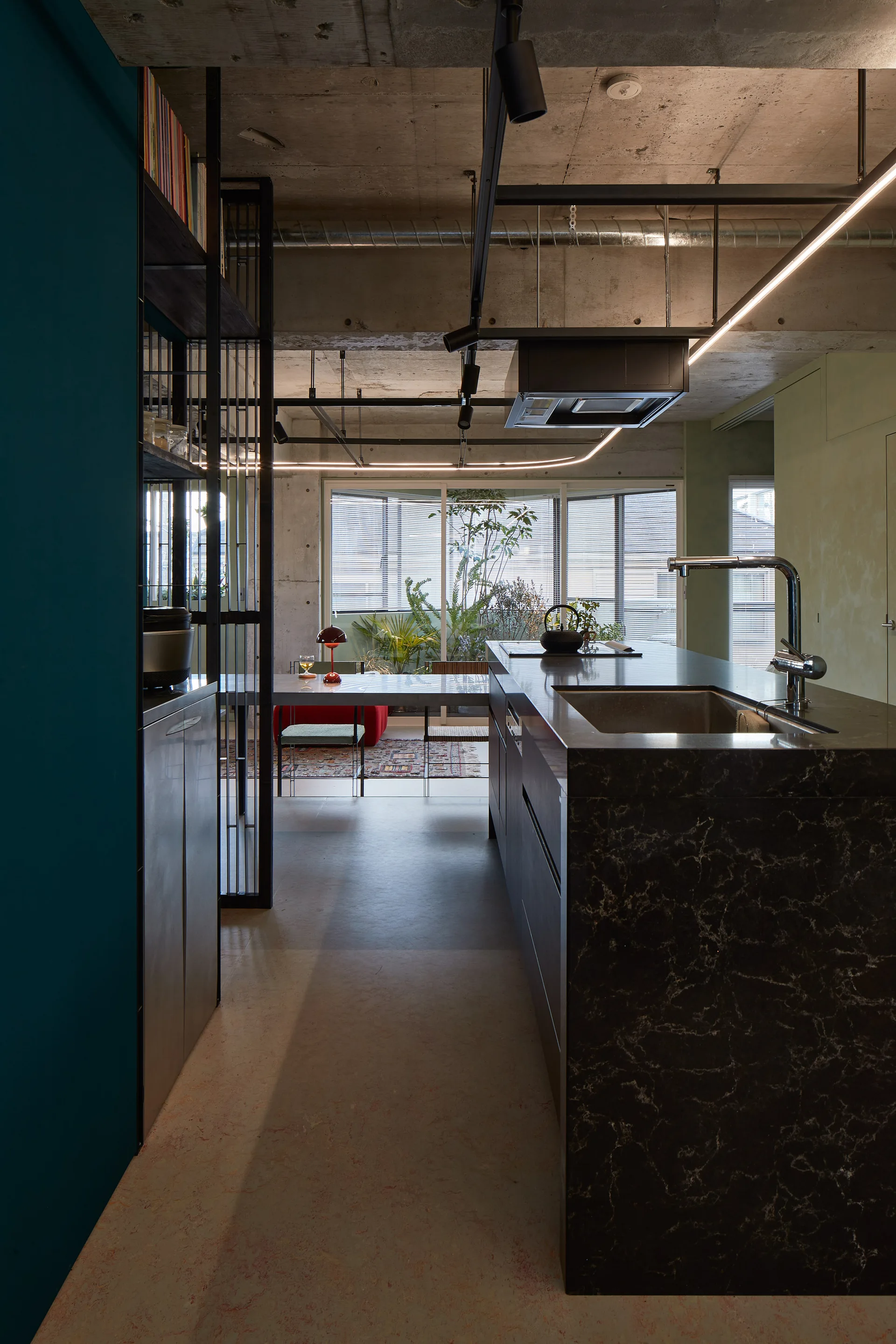 A modern kitchen featuring a dark veined stone island, a metal frame room divider, and an exposed concrete ceiling with track lighting.