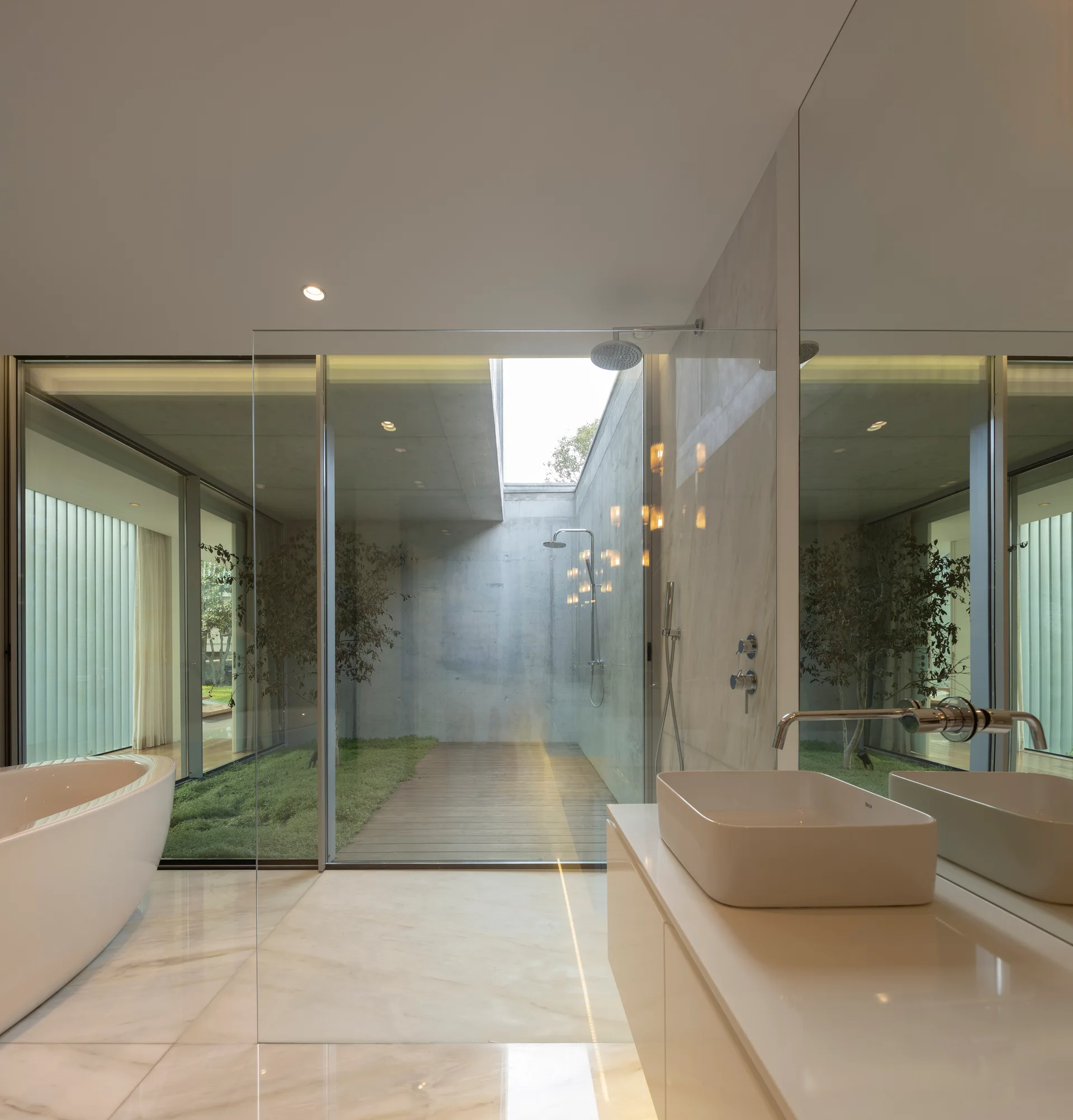 A modern white bathroom featuring a freestanding bathtub, a vessel sink vanity, and a large mirror facing a glass-walled internal courtyard.
