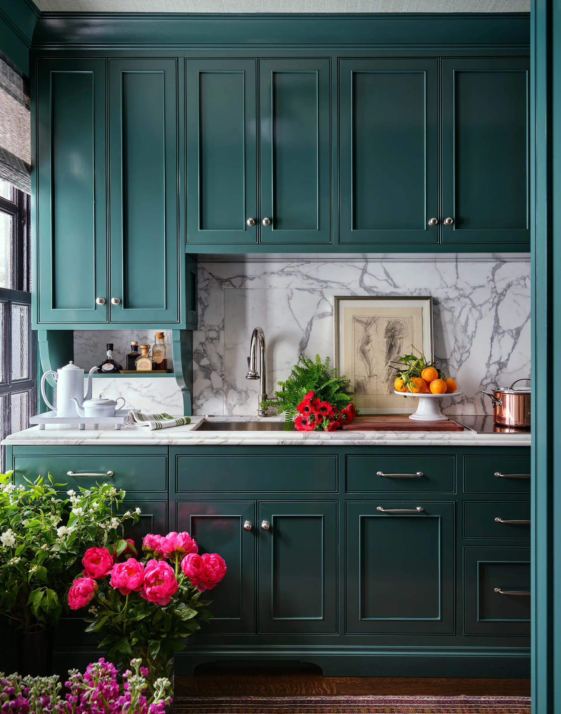 A kitchen features deep green shaker-style cabinets, a polished white marble countertop and backsplash with grey veining, and a stainless steel faucet.