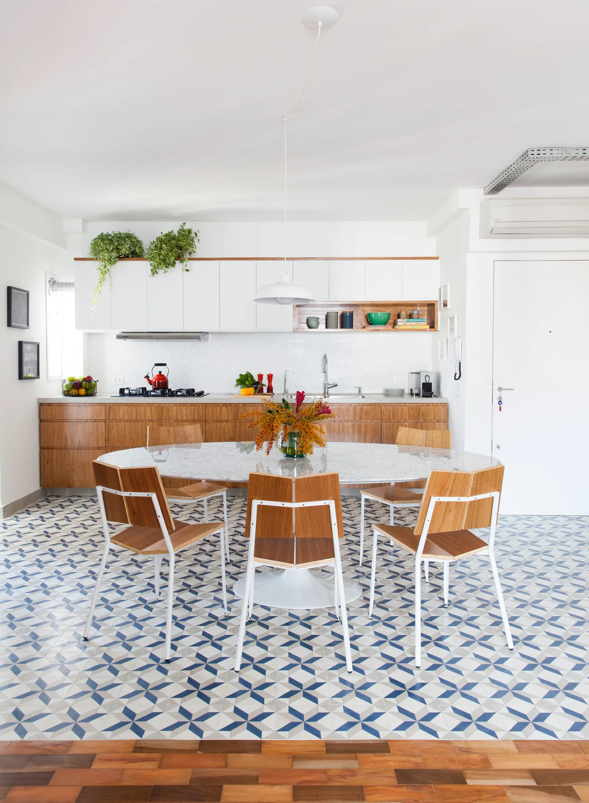 A modern kitchen and dining area with patterned blue and white floor tiles, a marble oval table, wood chairs, and wood-toned lower cabinets.