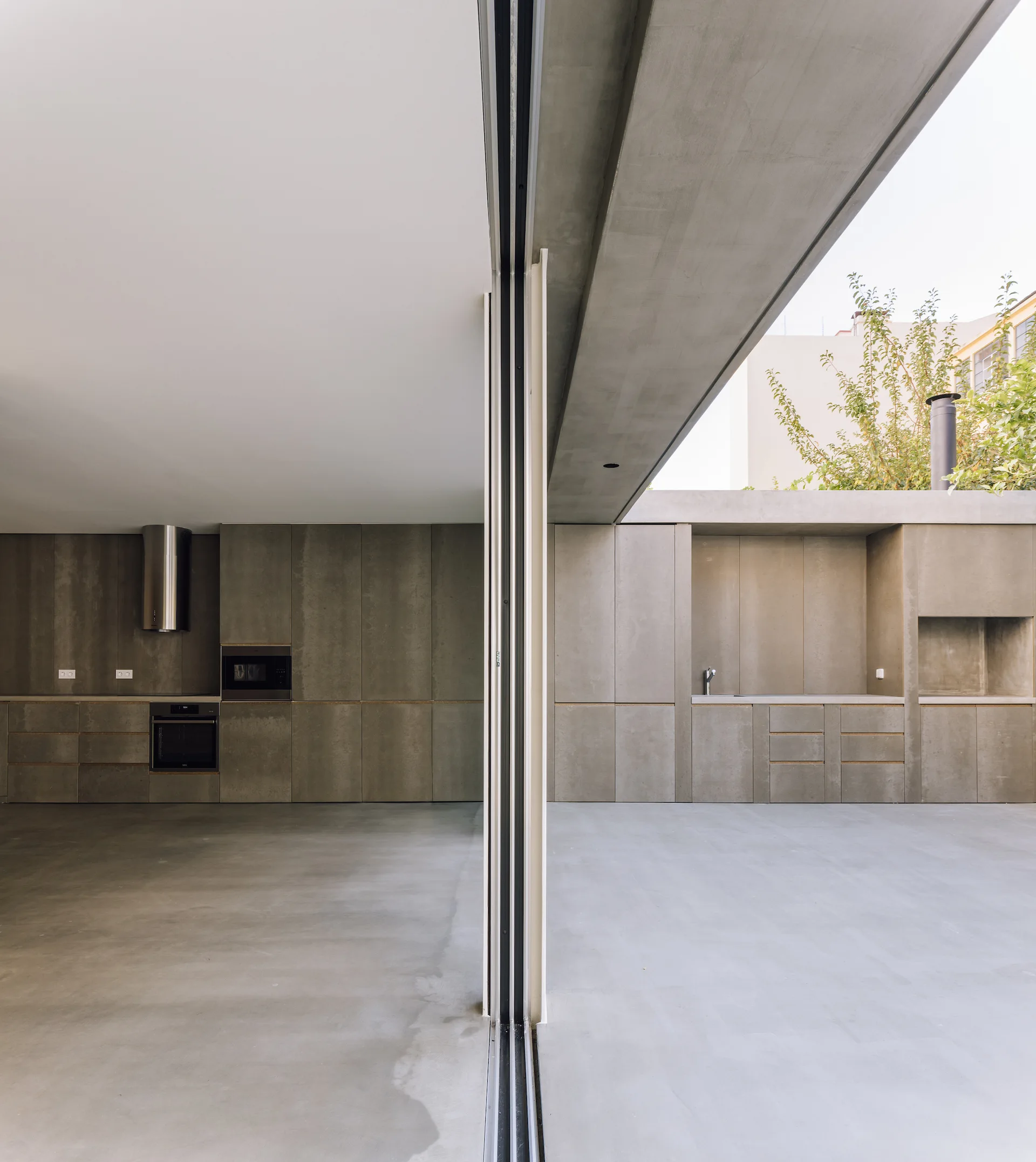 A minimalist kitchen with grey concrete cabinets and smooth floors opens up to an outdoor cooking area through a sliding glass door.
