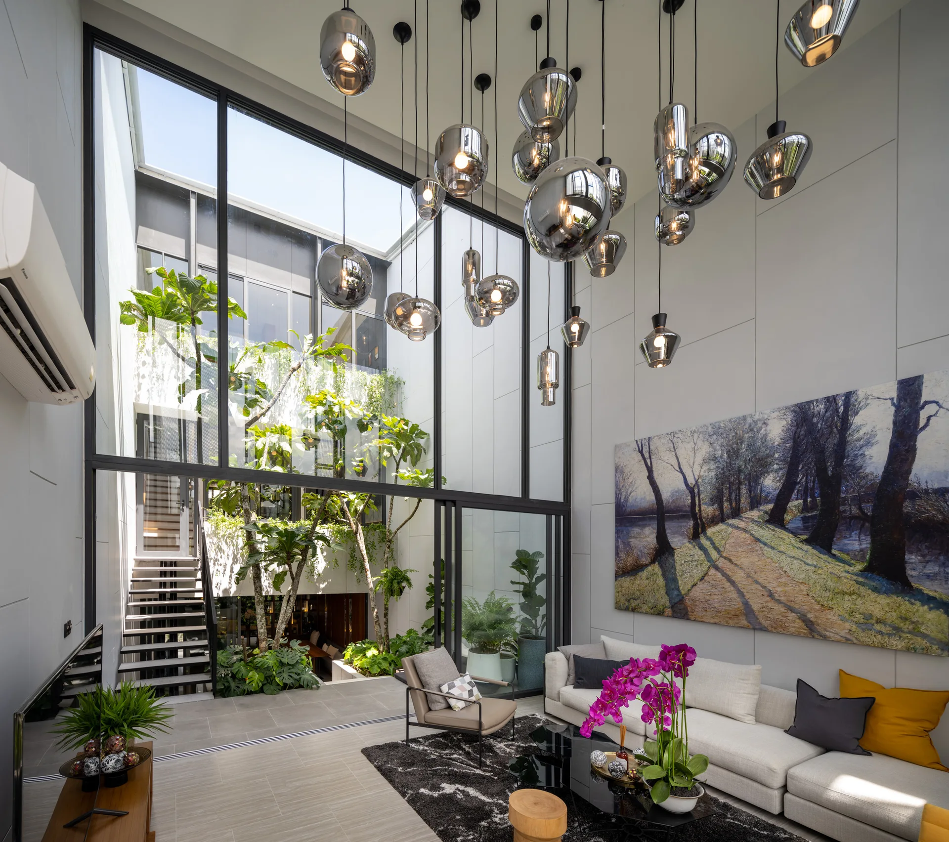A modern living room features a cluster of silver globe pendant lights, a white sectional sofa, and a large glass wall opening to a leafy courtyard.
