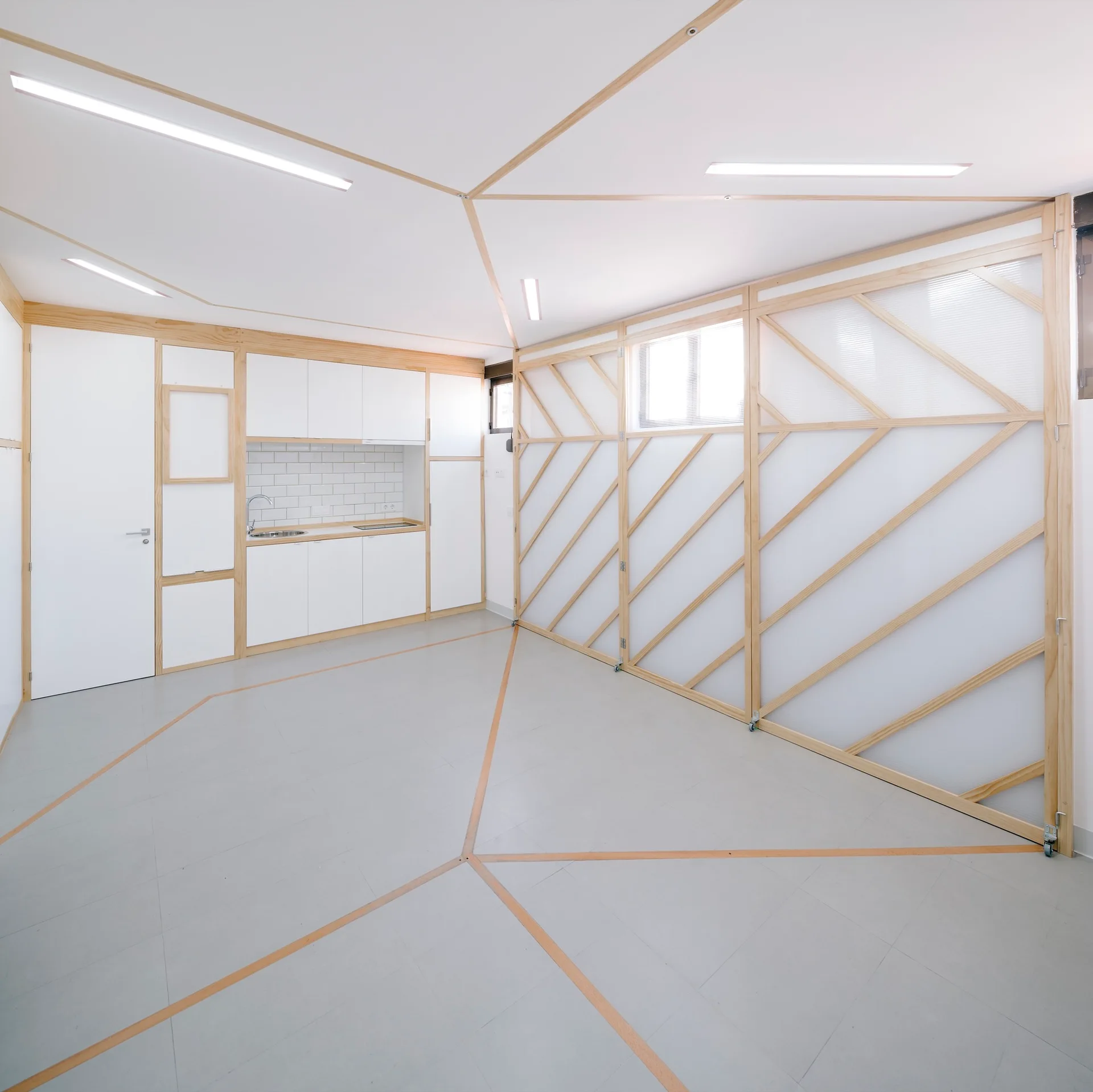 A minimalist white kitchen features geometric wood-lined patterns on the gray floor and white ceiling, alongside a large wood-framed translucent sliding screen.