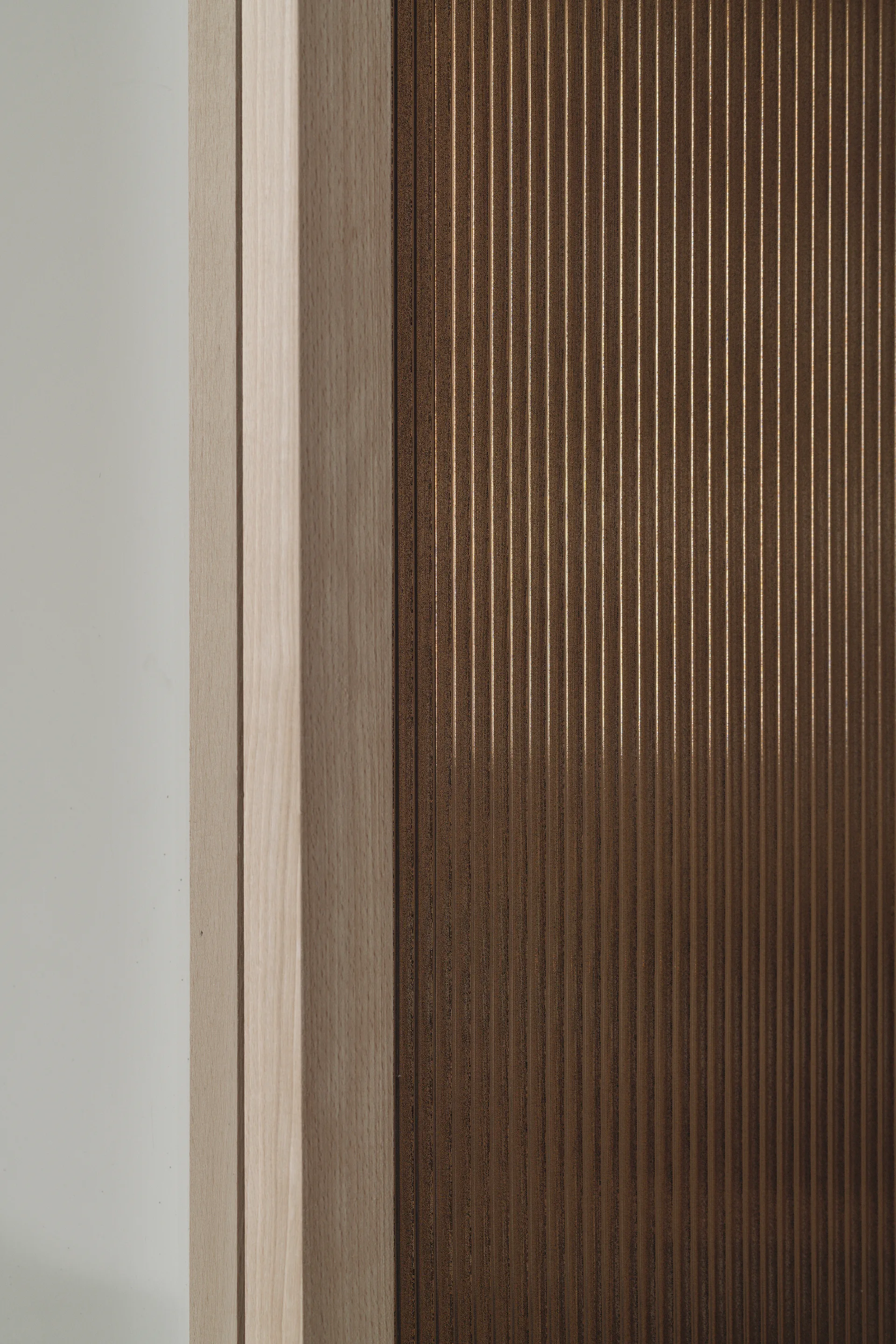 A close-up detail of fluted dark brown wall paneling bordered by light natural wood trim against a plain white wall.