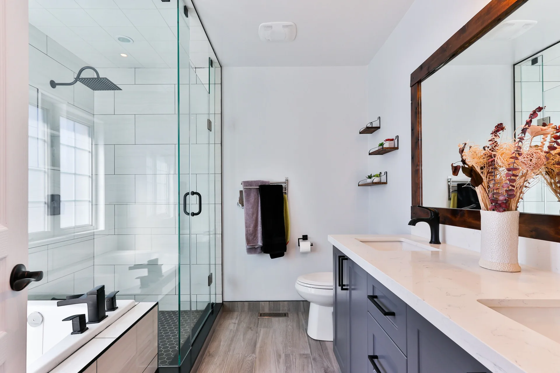 A contemporary bathroom features a dark gray vanity with a stone-like countertop, a glass-enclosed walk-in shower, and wood-look flooring.