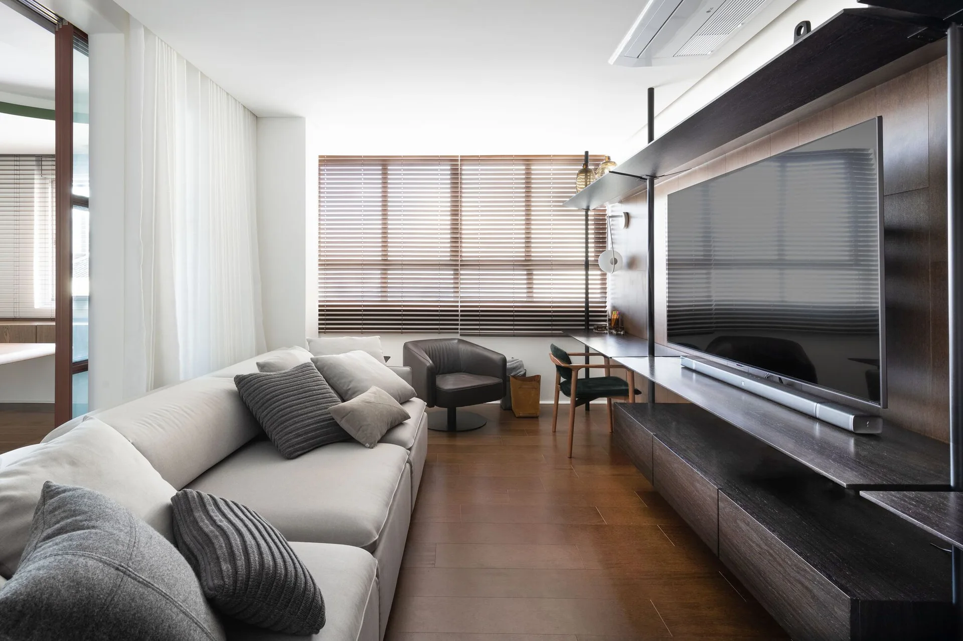 A contemporary living room features a long light gray sofa opposite a dark wood built-in media console with an integrated desk and flat-screen TV.
