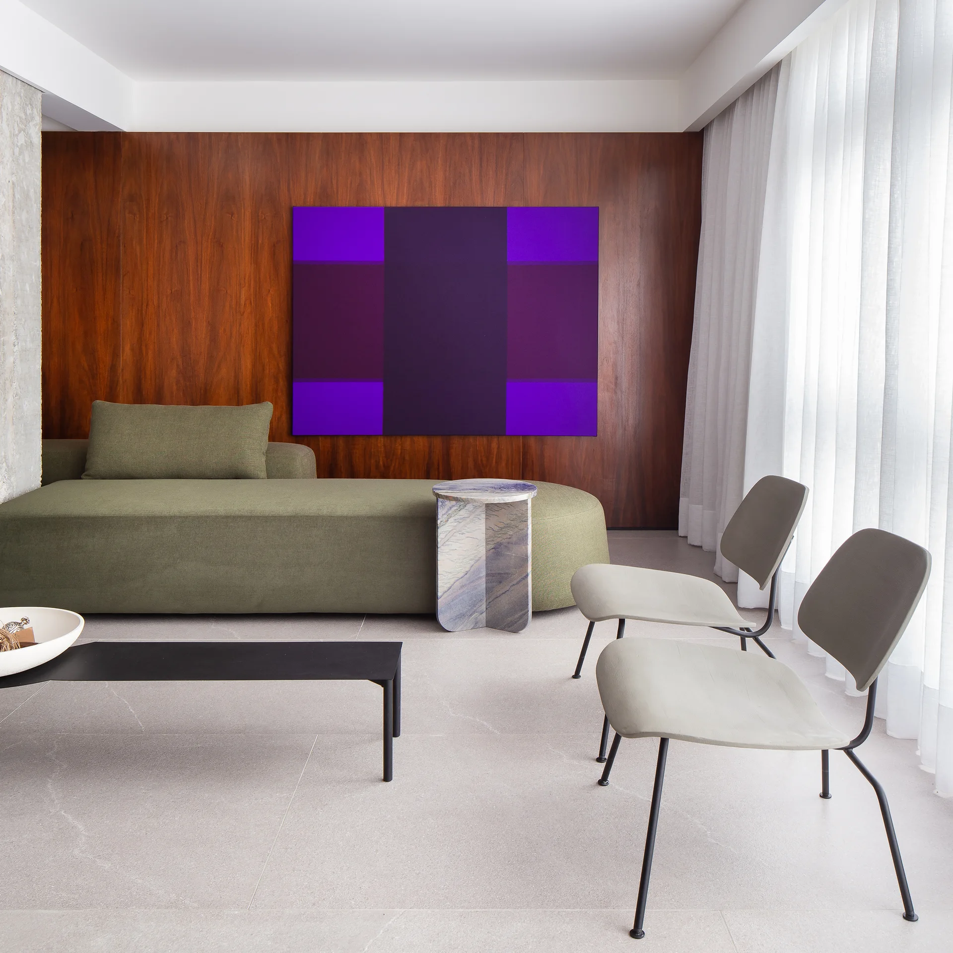 A modern living room features a green low-profile sofa, two gray chairs, a stone side table, and a large purple abstract painting on a wood-paneled wall.