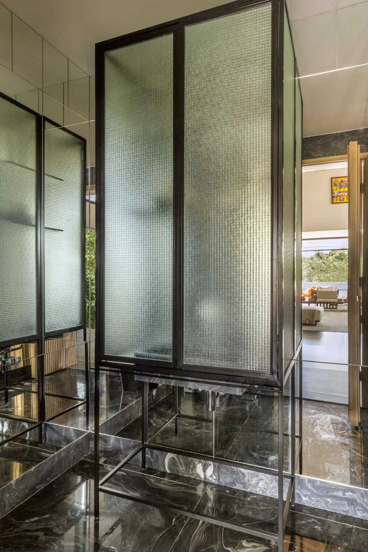 A modern bathroom featuring a black metal-framed vanity with textured glass panels set against a mirrored wall and dark, polished marble flooring.