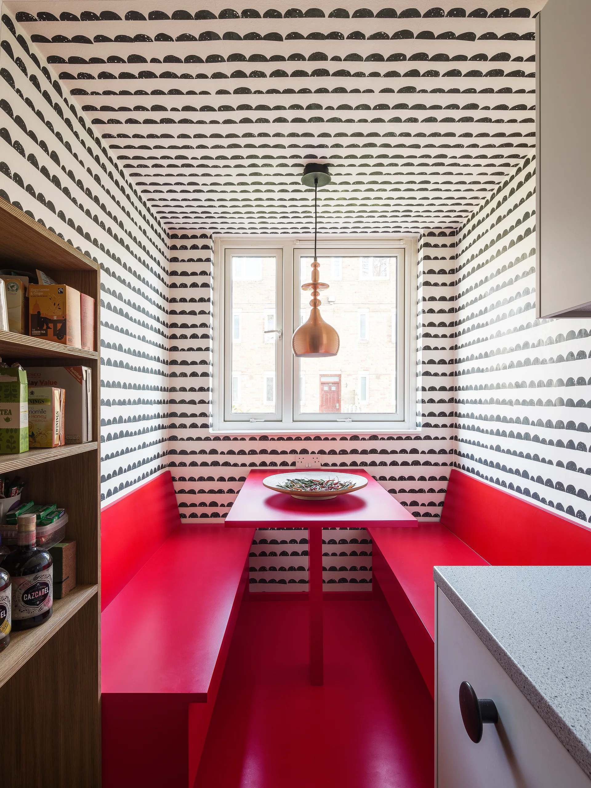 A small dining nook features red benches and a matching table set against black and white patterned wallpaper that extends onto the ceiling.