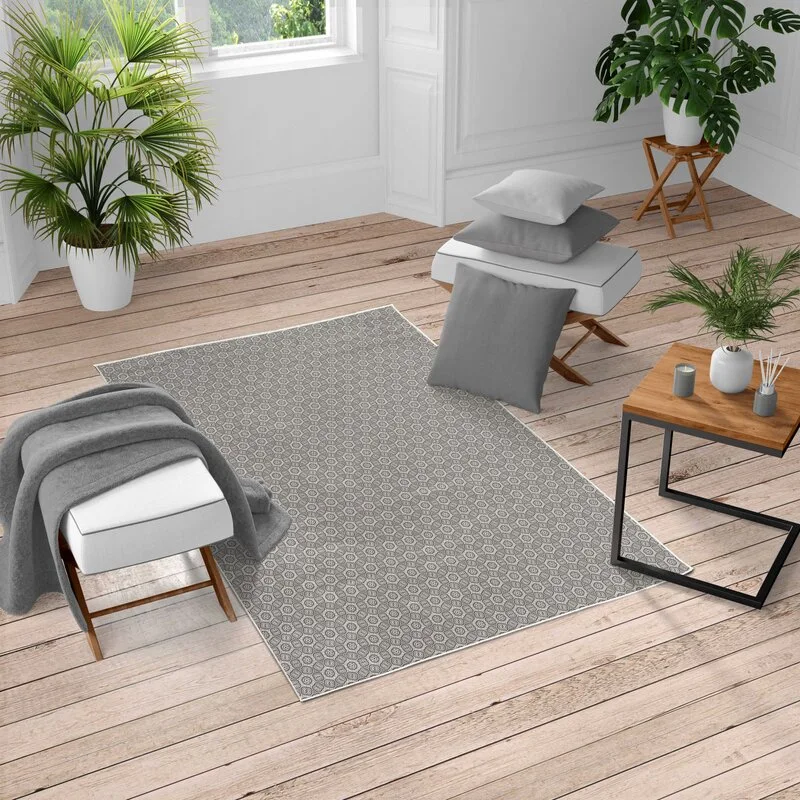 A gray geometric patterned rug lies on a light wood plank floor in a bright room with white paneled walls and minimalist white benches.