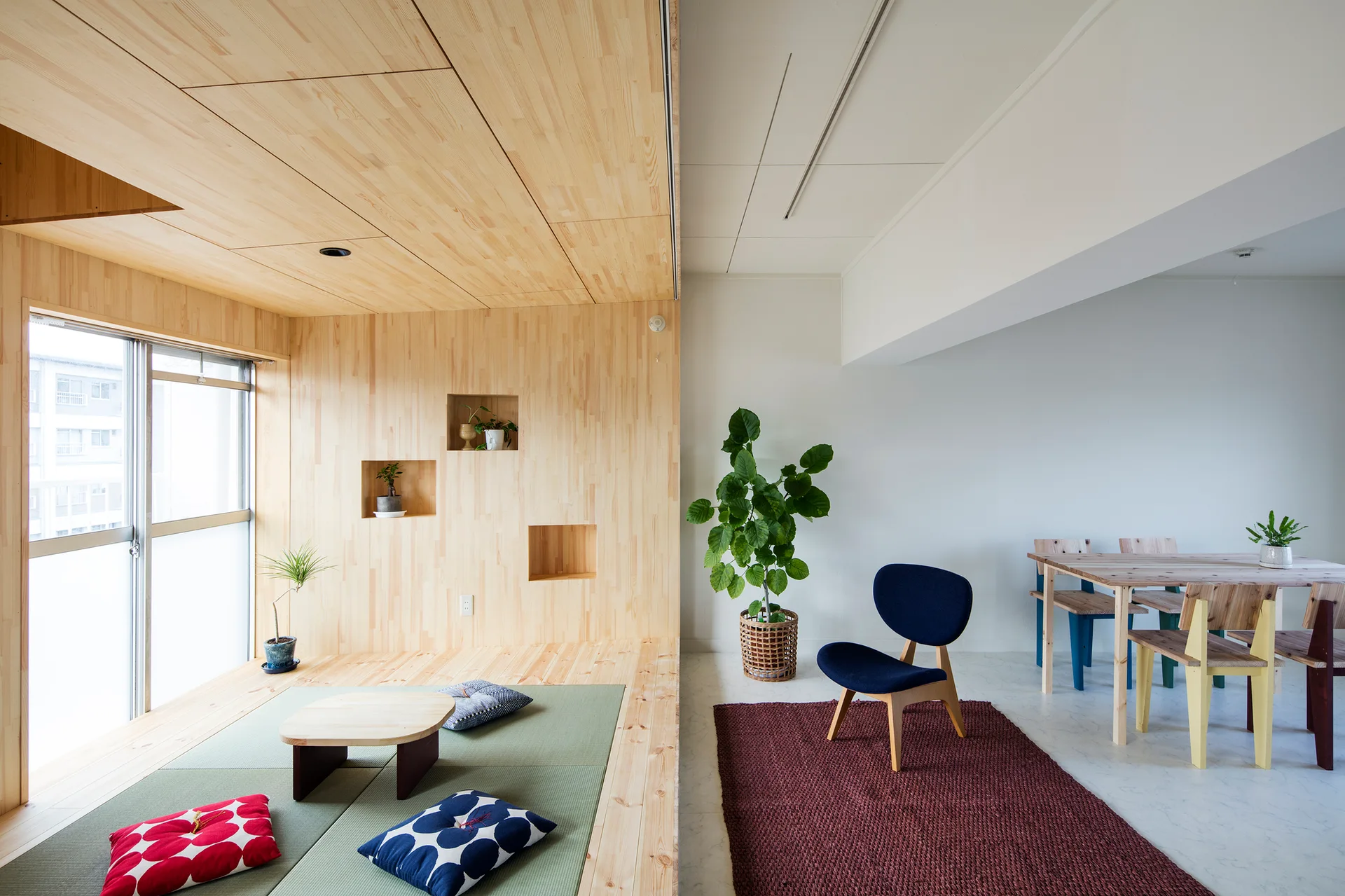 A modern split-level room features a raised wooden platform with green tatami mats, built-in wall niches, and an adjacent dining area.