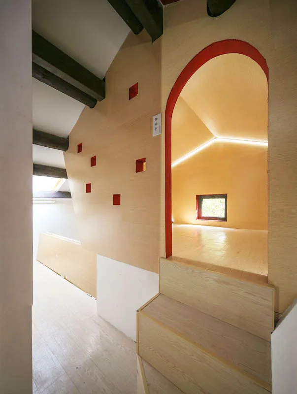 A wood-paneled attic staircase leads to an arched doorway highlighted with bright red trim and small square wall niches.
