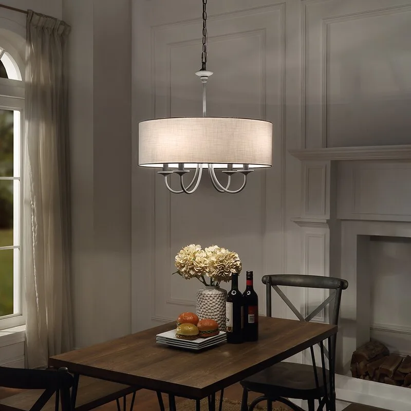 A dark wood dining table is set under a large grey fabric drum chandelier, with a white paneled fireplace in the background.