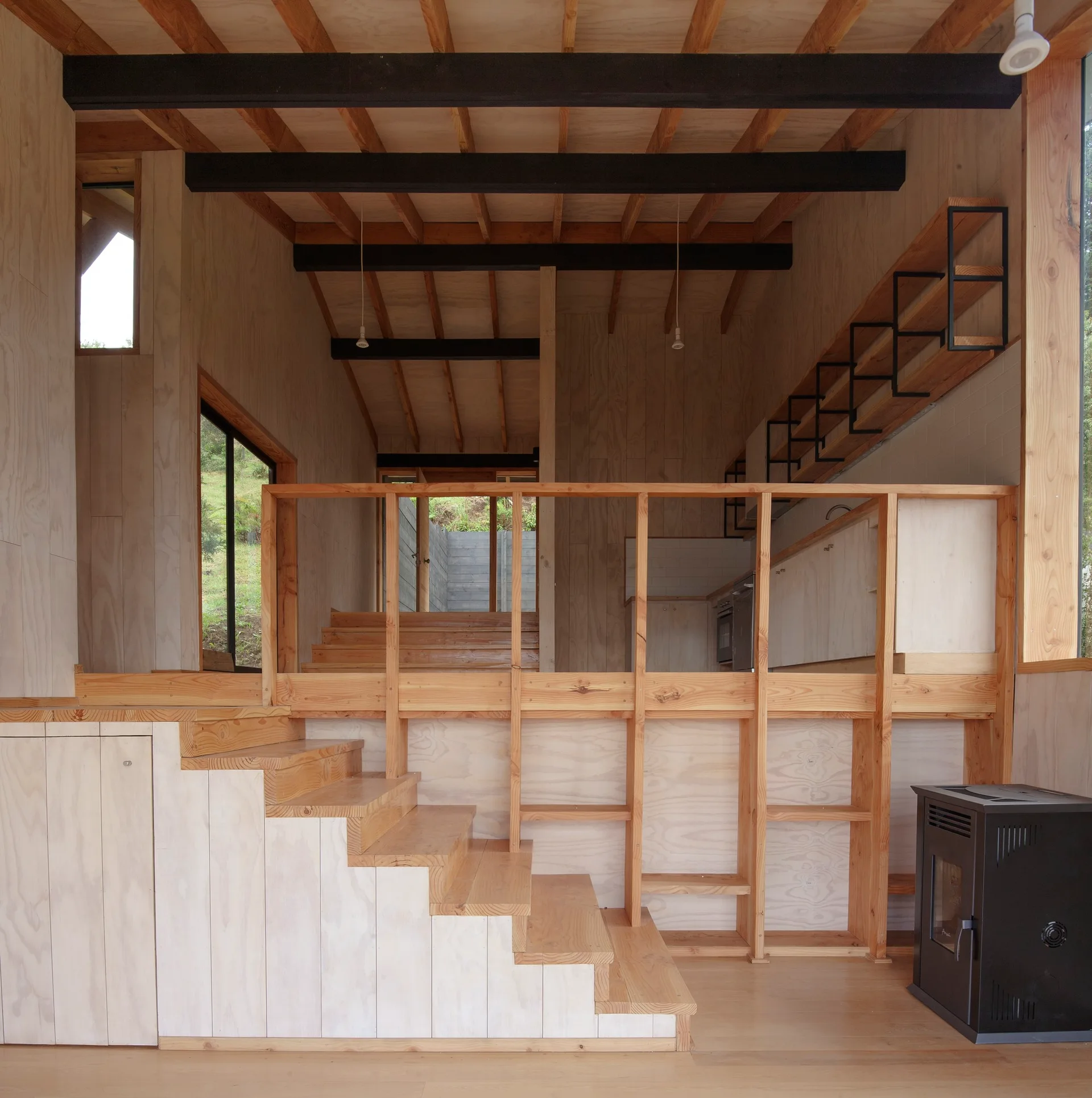 A split-level cabin interior features light plywood wall paneling, a wooden staircase, and dark exposed ceiling beams.