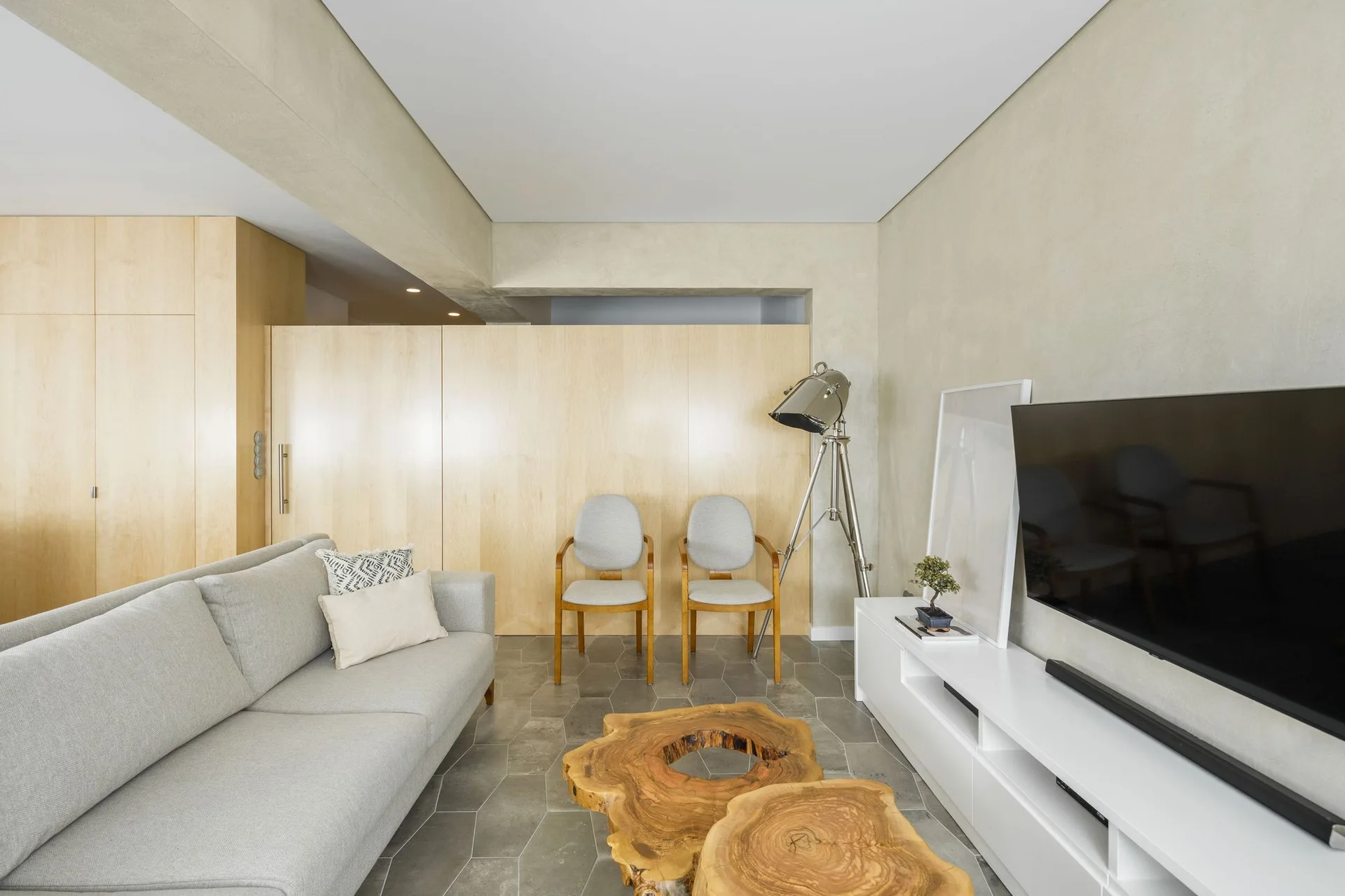 A grey couch sits opposite a white television console in a room with hexagonal floor tiles, wood wall panels, and two wooden coffee tables.