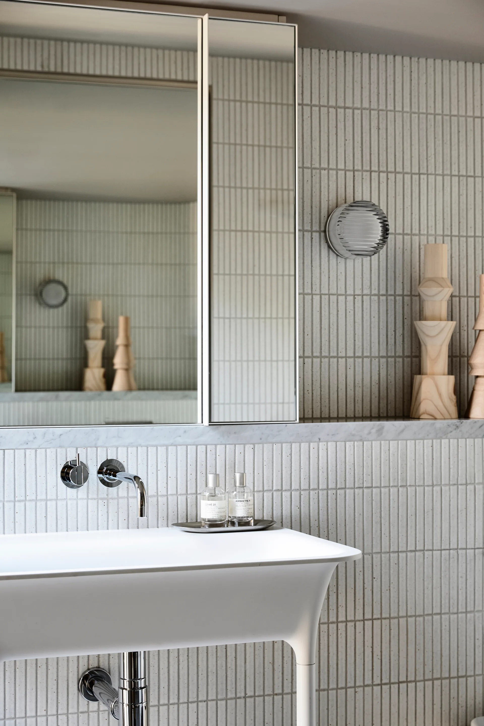 A minimalist bathroom sink vanity featuring a white console basin, wall-mounted chrome faucet, and vertically stacked textured off-white wall tiles.