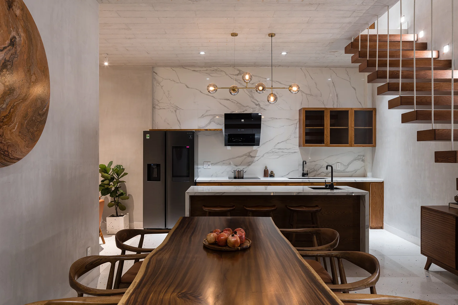 A modern kitchen and dining space with a live-edge wood dining table, marble-topped island, and open floating wooden stairs.