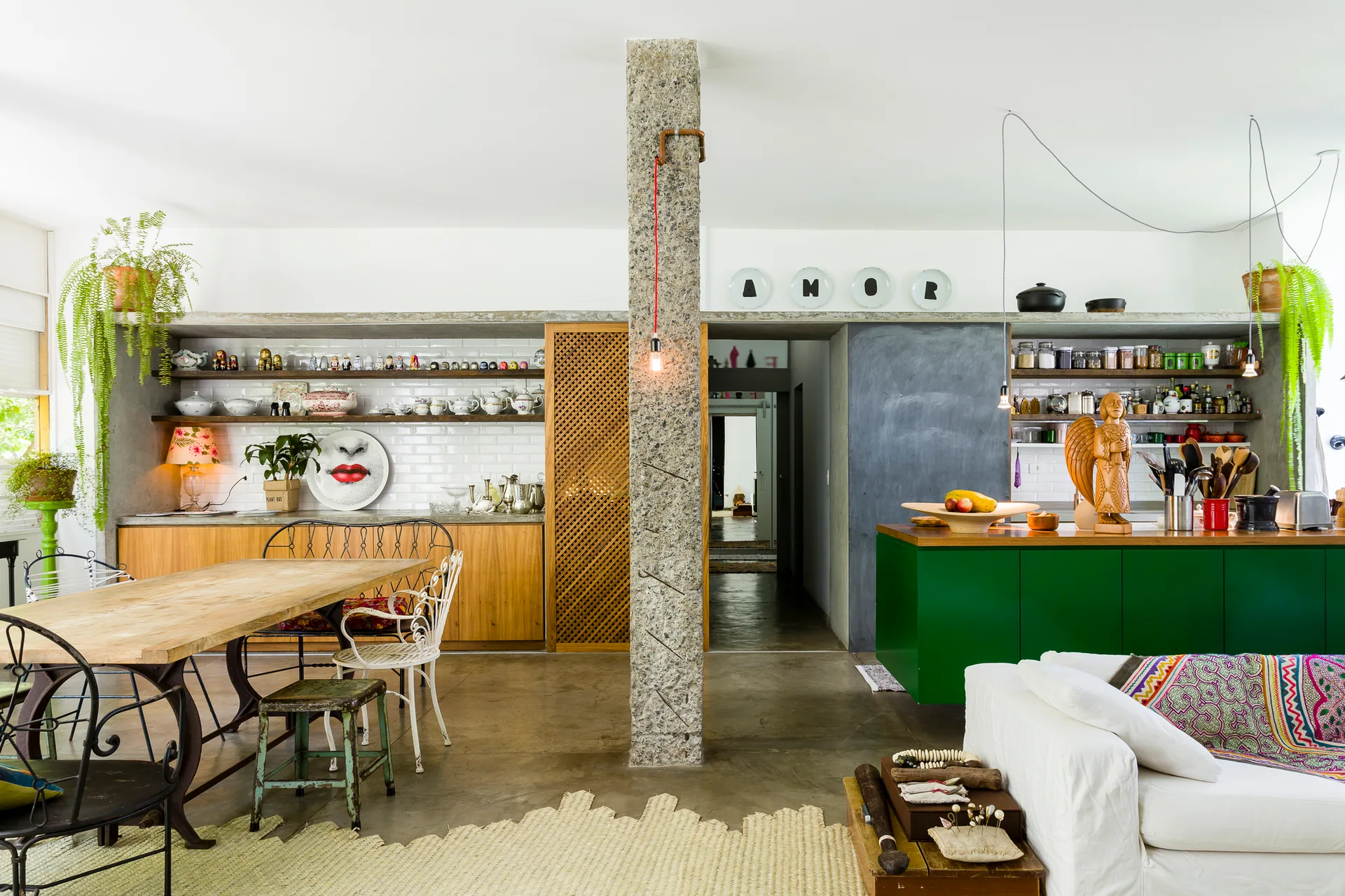 An open-concept kitchen and dining area featuring a prominent central stone column, a green kitchen island, and a wooden dining table with eclectic chairs.