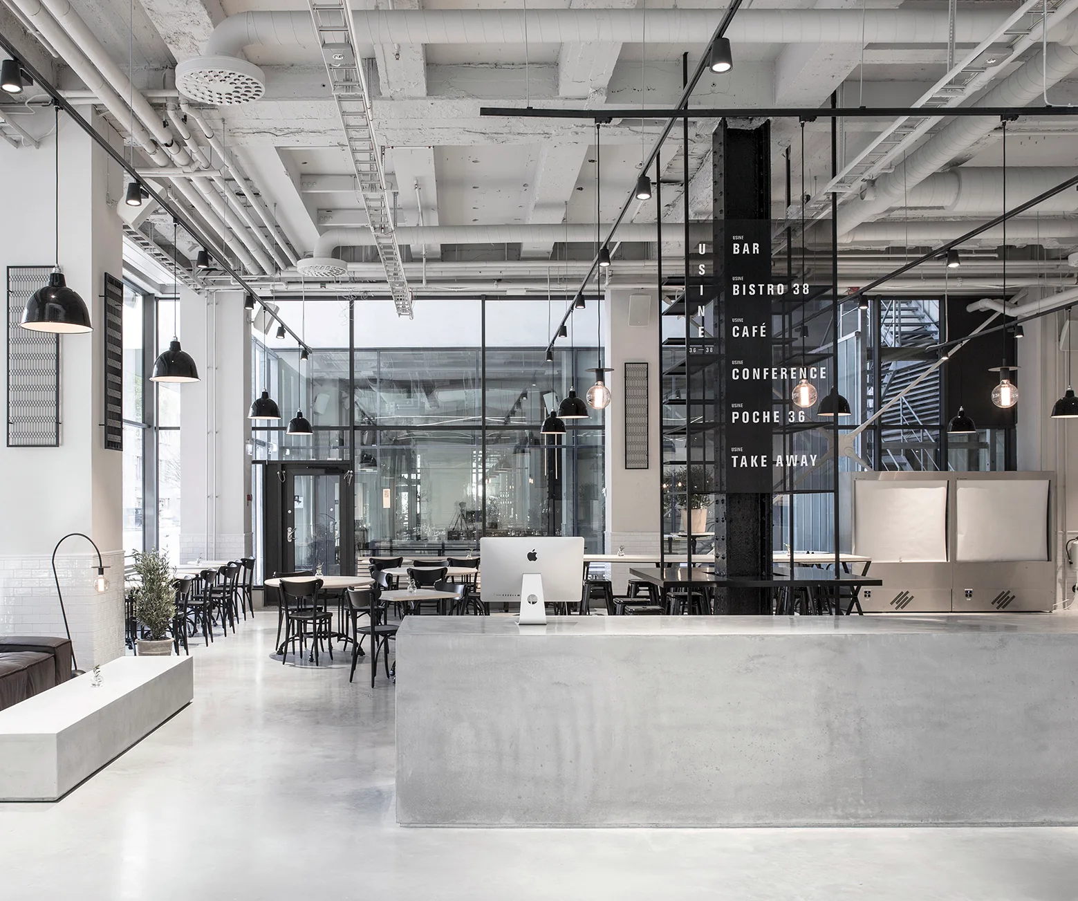 A spacious industrial cafe interior features a smooth grey concrete service counter, black pendant lights, and an exposed white pipe ceiling.
