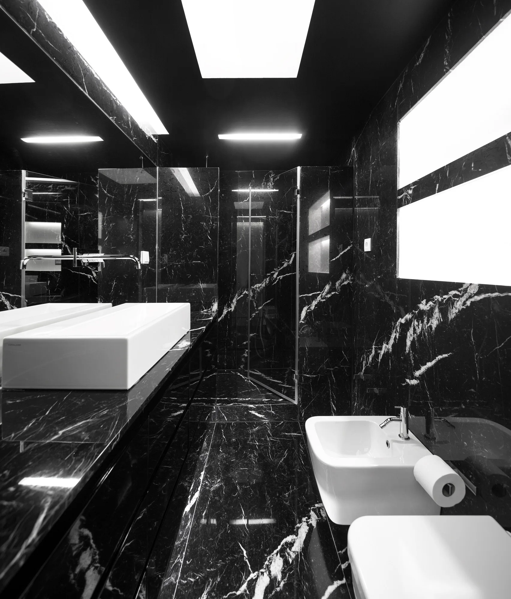 A modern bathroom lined with highly polished black marble featuring white veining, a white rectangular sink, and a matching bidet.