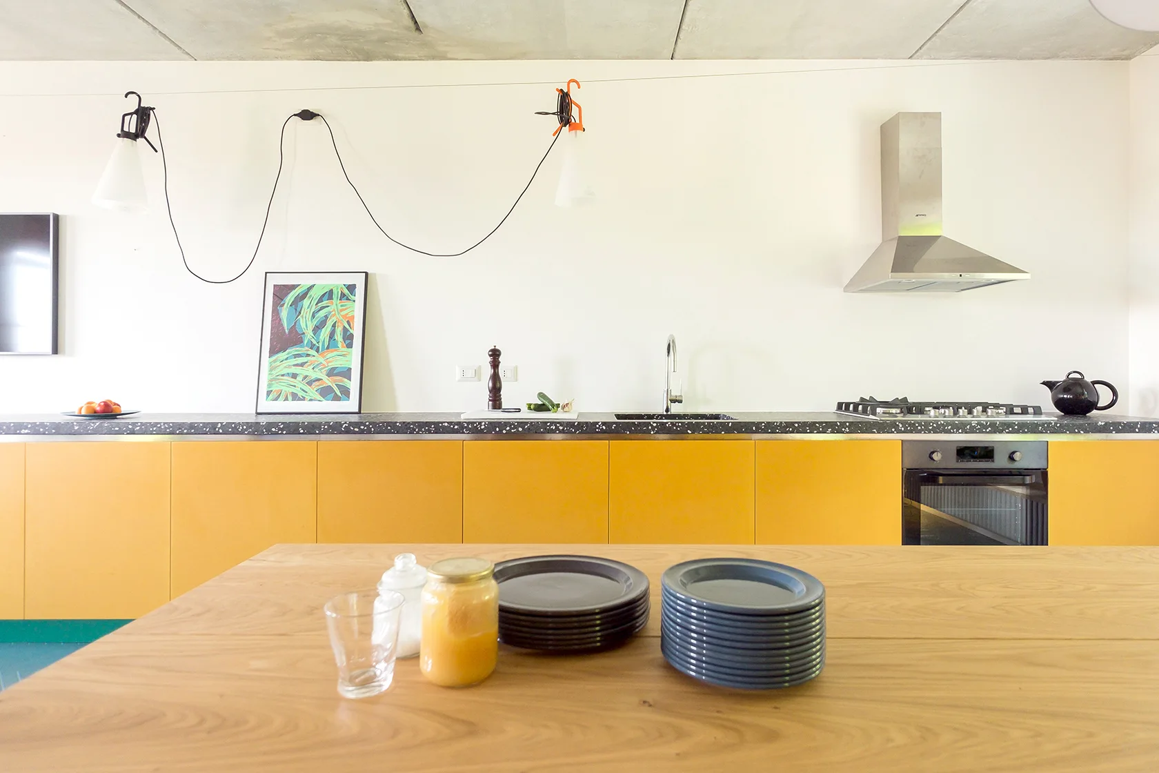 A modern kitchen featuring vibrant yellow lower cabinetry, a dark speckled countertop, and a wooden dining table in the foreground.