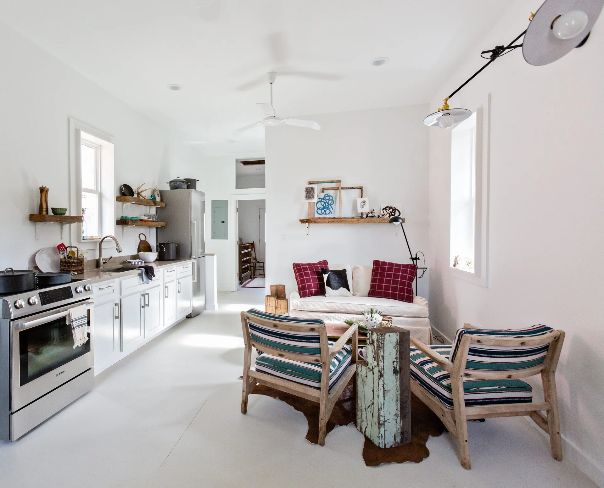 An open plan kitchen with white cabinets is adjacent to a living space featuring a cream sofa, striped armchairs, and a cowhide rug.