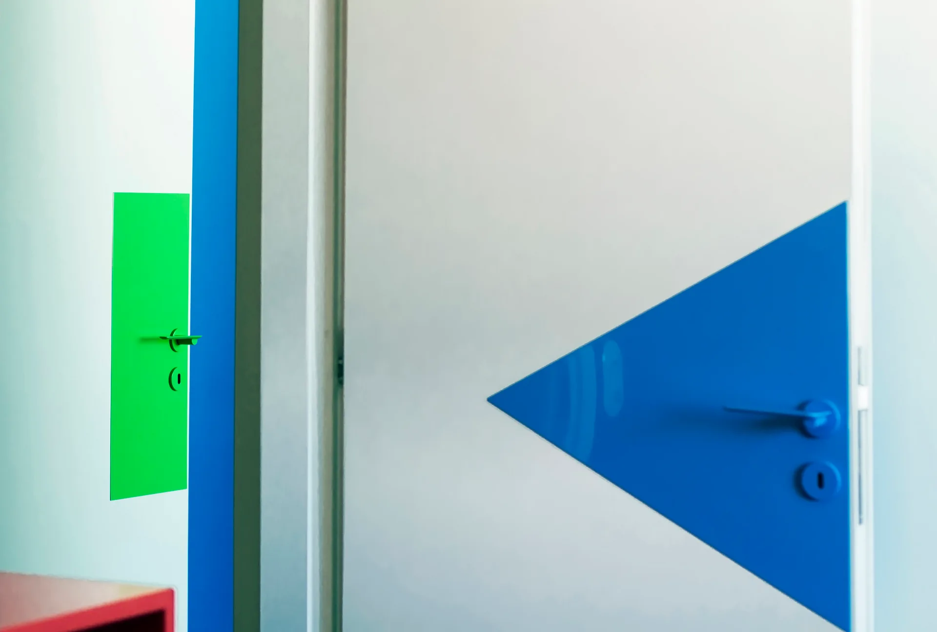 Modern interior doors feature a bright blue triangular plate and a vivid green rectangular plate around minimalist door handles.