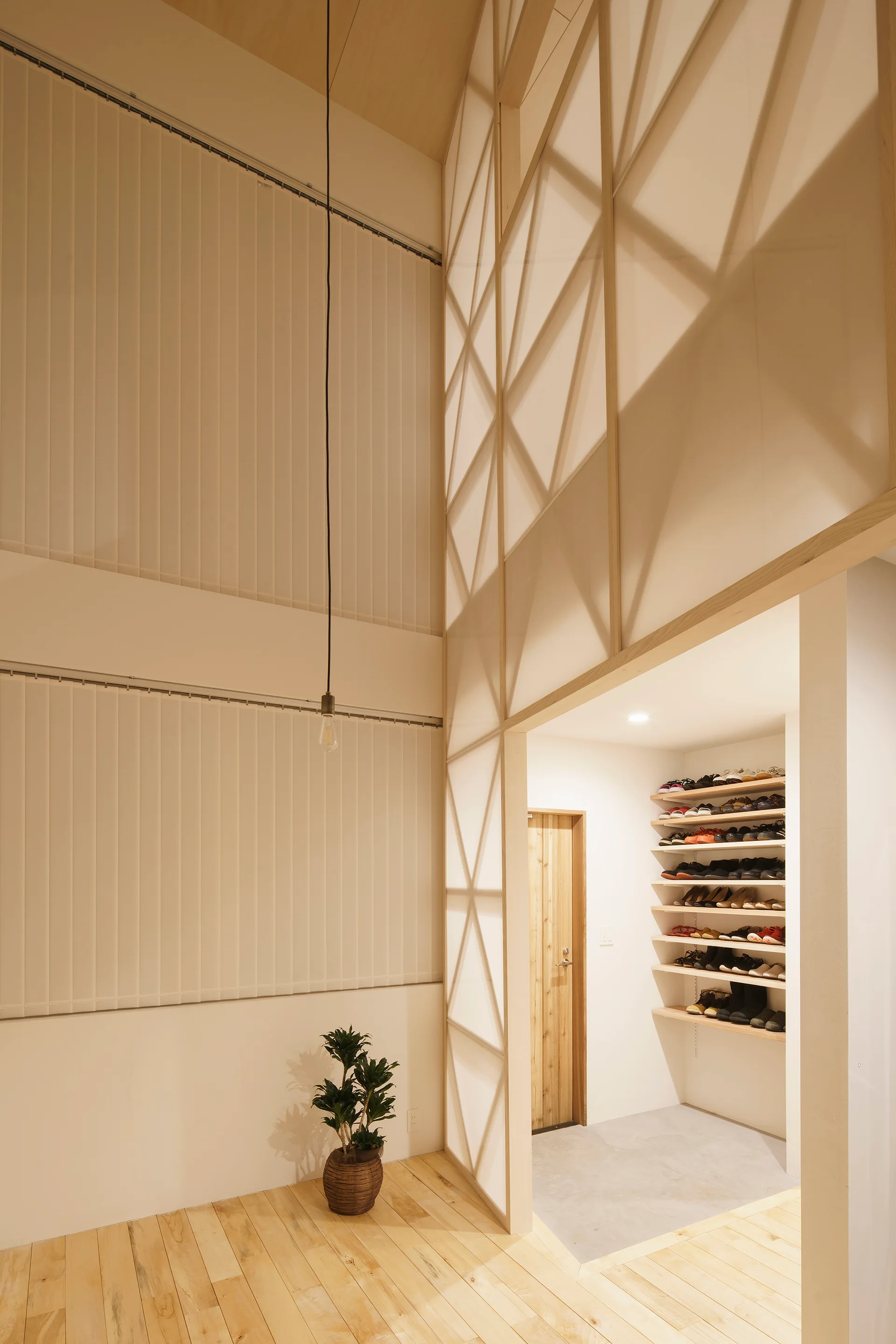 A modern minimalist entryway features a translucent geometric partition, light wood flooring, and an alcove filled with open wooden shoe shelving.