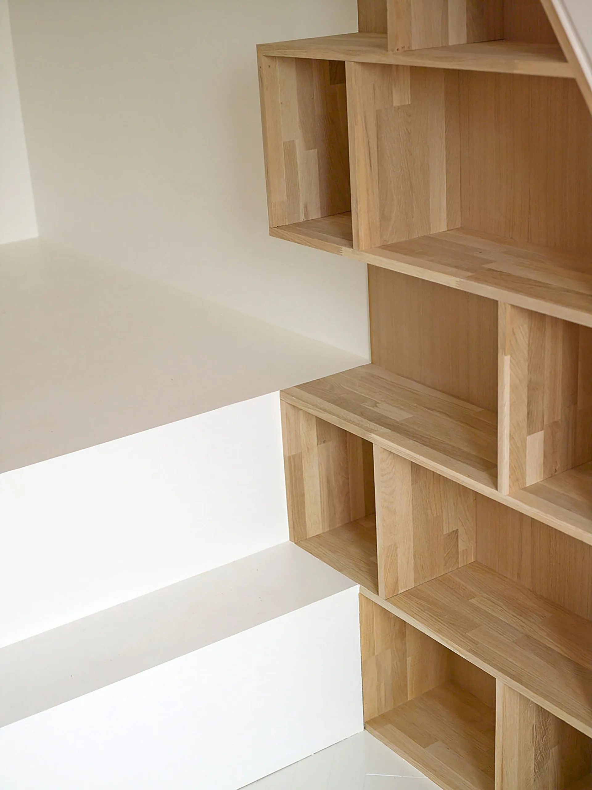 A minimalist white staircase next to a built-in light wood shelving unit with open rectangular cubbies.