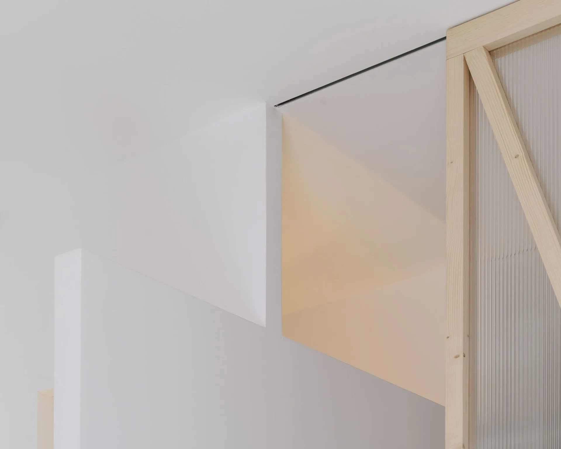 A minimalist white stepped wall stands next to a light wood framed partition with textured reeded glass.