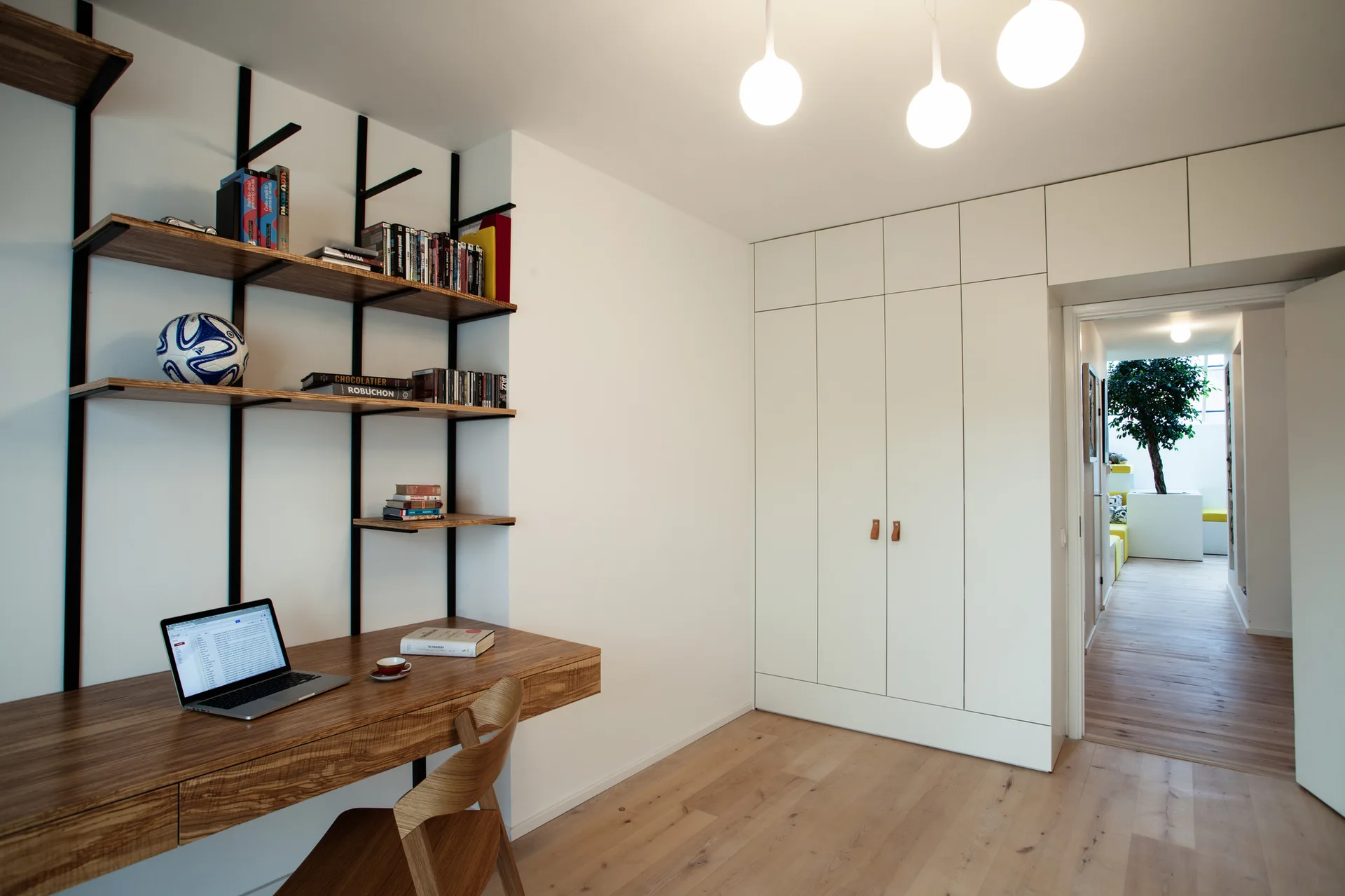 A modern workspace features a floating wood desk, black-framed open shelves, and tall white built-in storage cabinets.