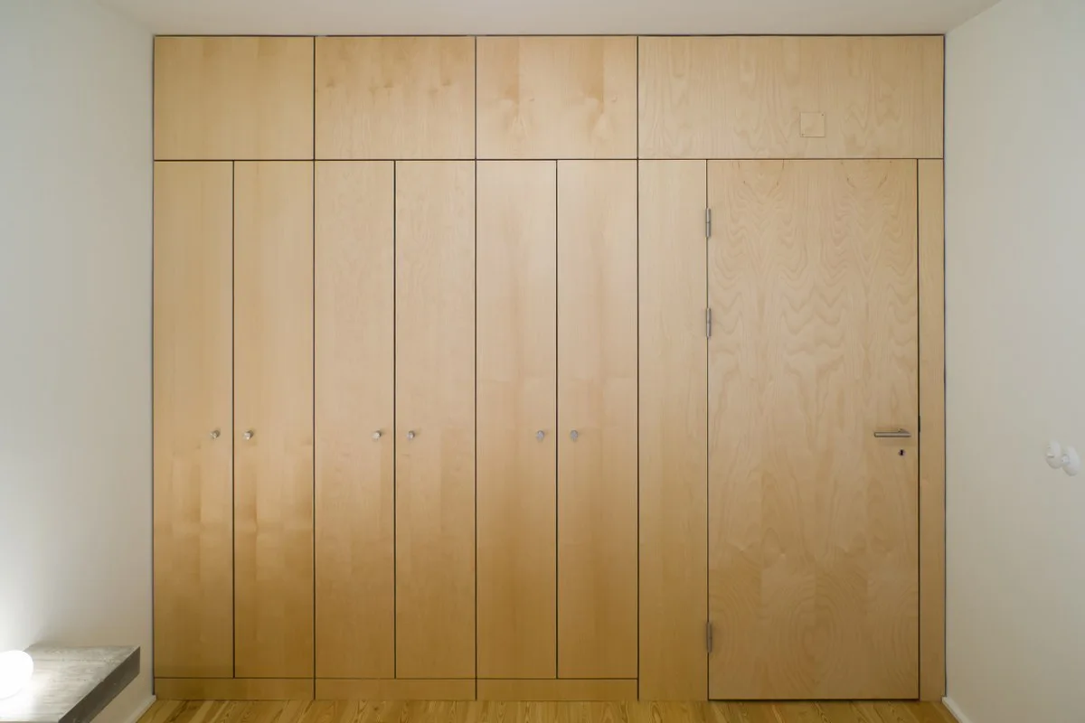 A floor-to-ceiling built-in storage unit made of light wood panels with an integrated flush door and small round knobs.