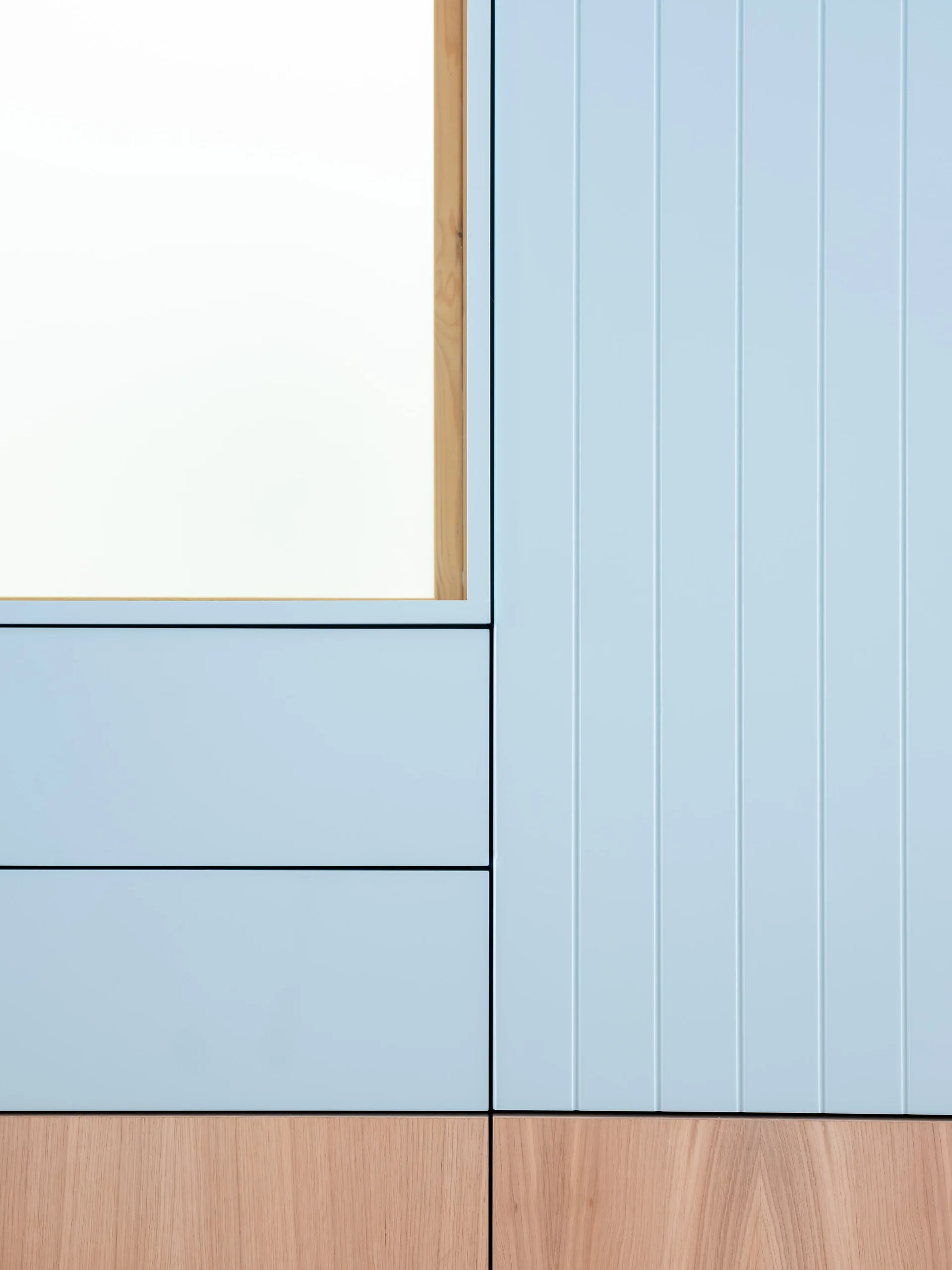 Matte light blue custom cabinets with vertical grooved paneling, smooth drawer fronts, and a natural wood base trim.