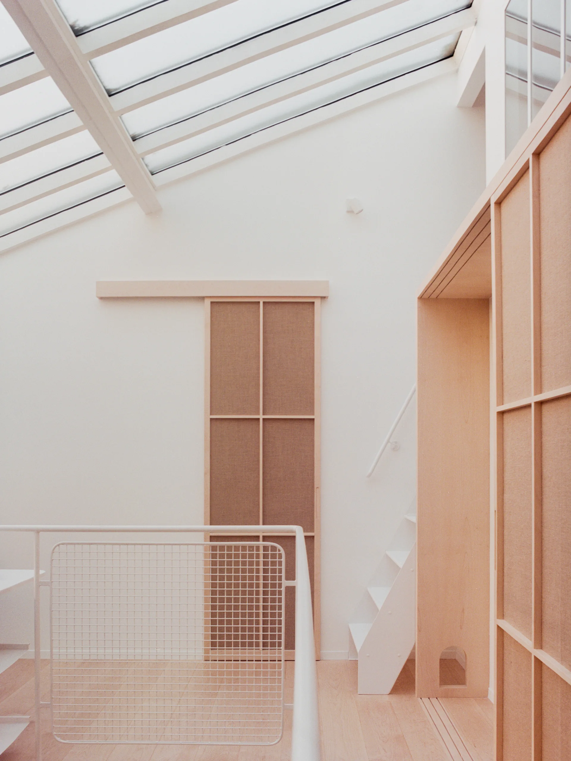 A bright loft landing featuring a slanted skylight, white walls, light wood sliding doors, and a minimalist white staircase.