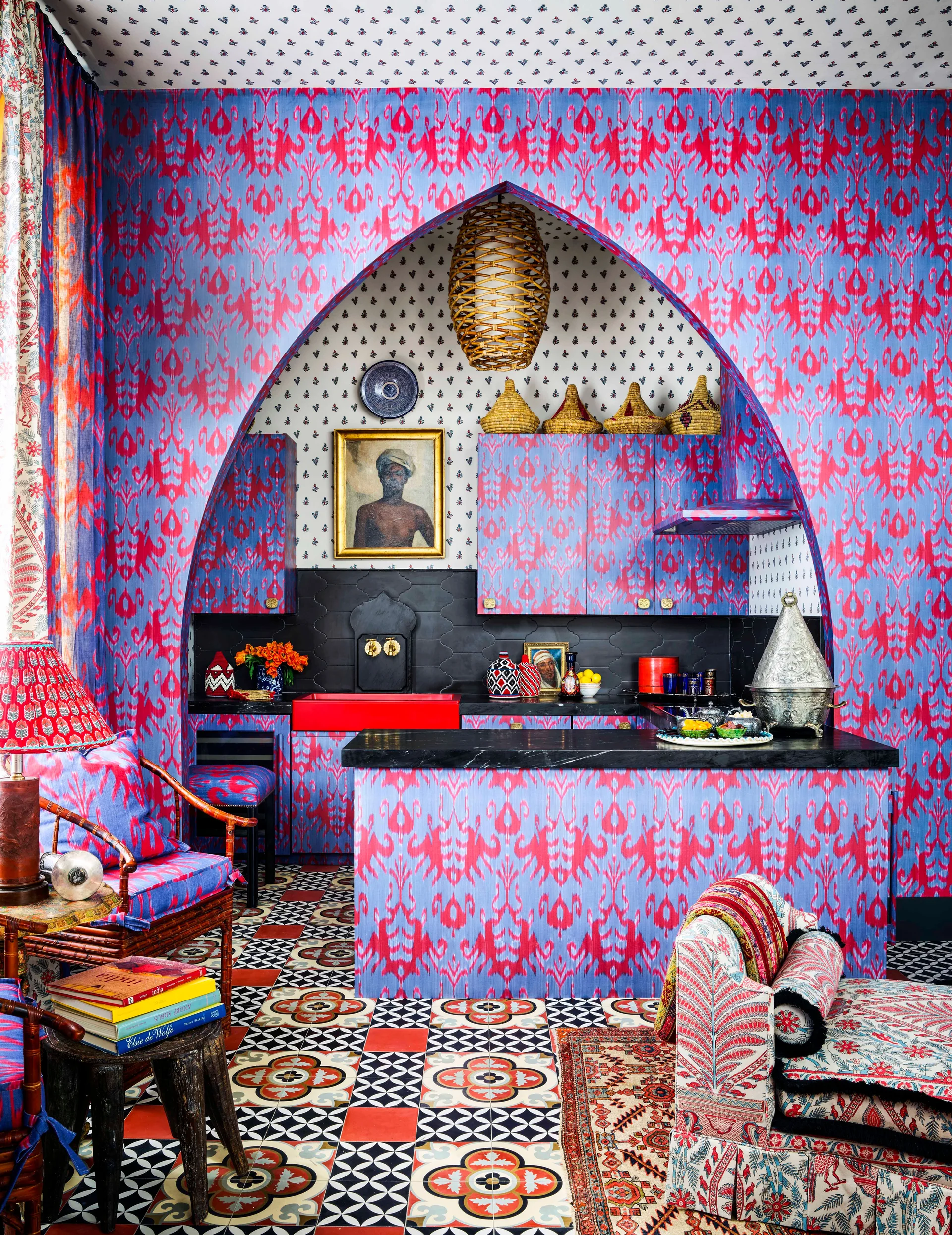 A maximalist kitchen features a pointed arch alcove, blue and fuchsia ikat patterned walls and cabinets, and a geometric encaustic tile floor.