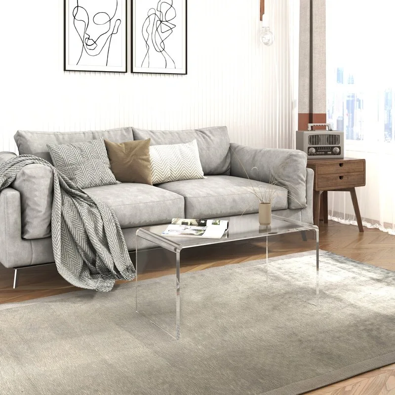 A grey fabric sofa and a clear acrylic coffee table sit on a textured grey rug over herringbone hardwood flooring.