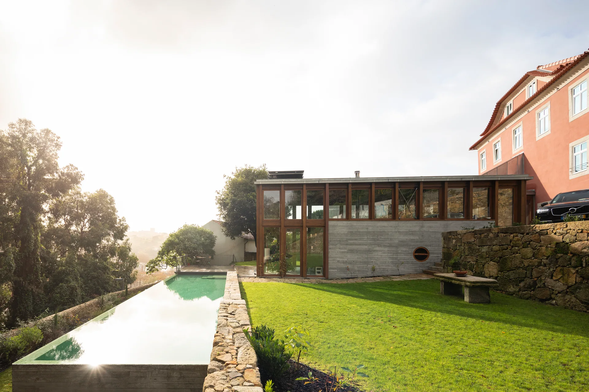 A long, narrow outdoor lap pool sits next to a green lawn and a modern concrete and glass home extension.