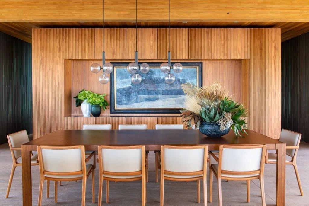 A dining room features a wood table, six cream chairs, and a vertical slatted wood accent wall with a recessed niche containing art.