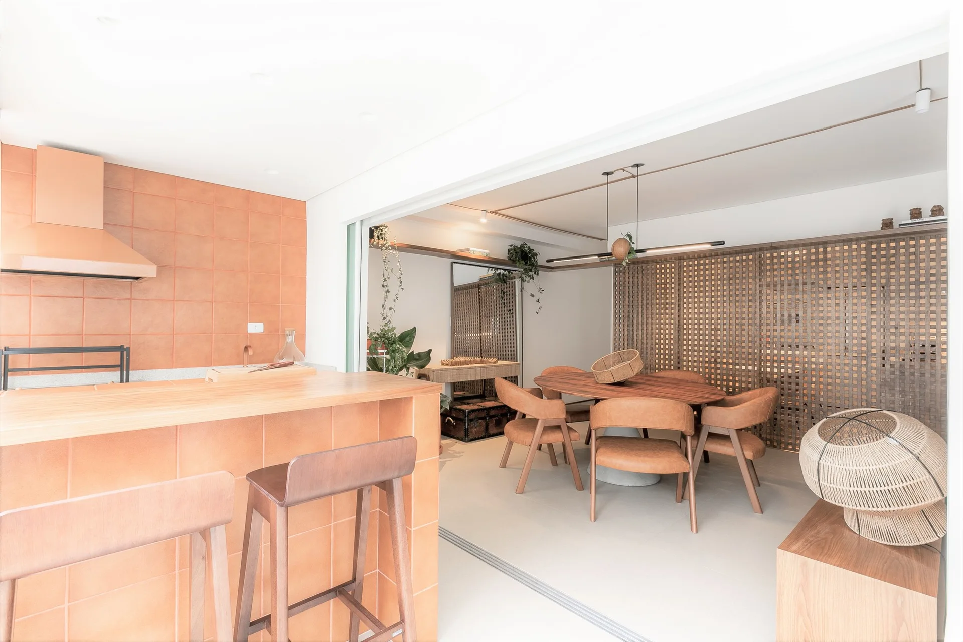 An open-plan dining room featuring an oval wooden table and leather chairs next to a kitchen island wrapped in square terracotta tiles.