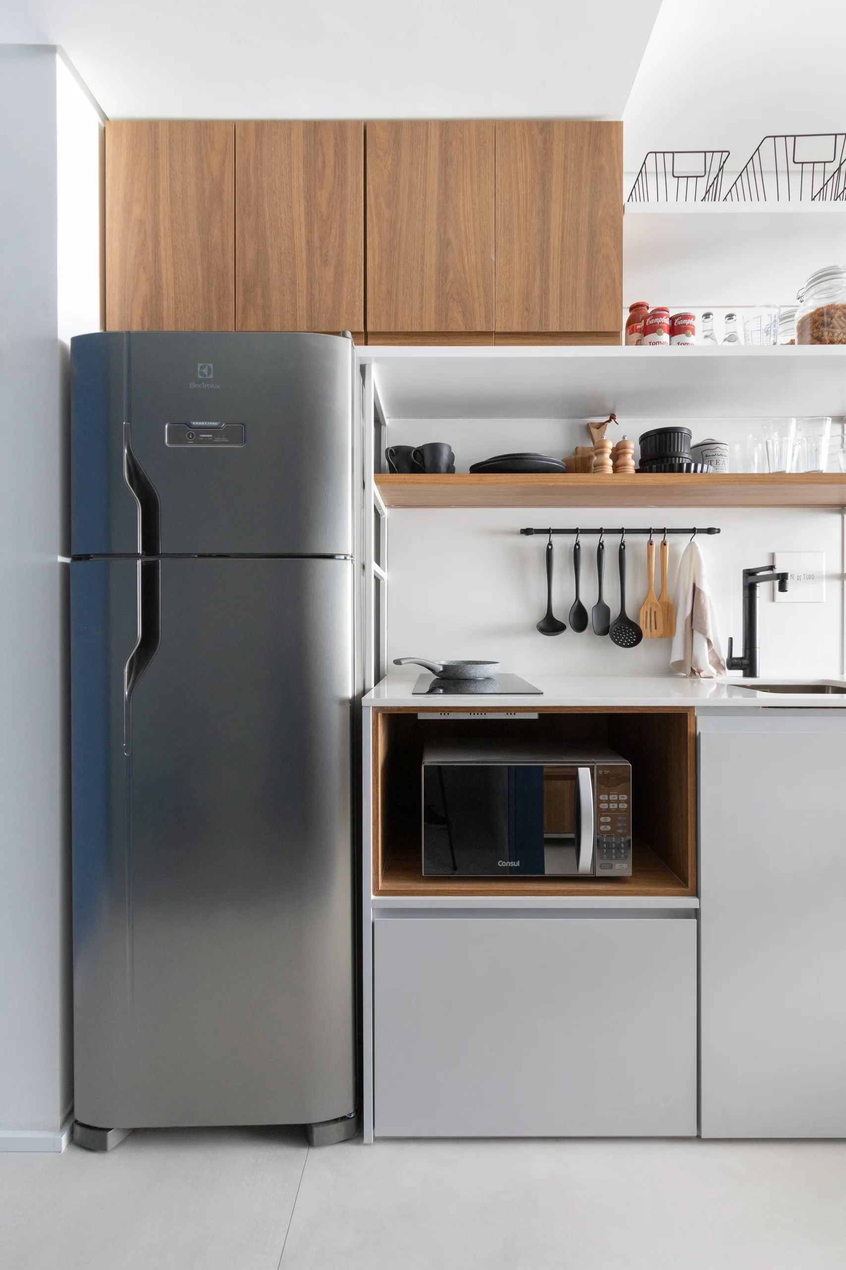 A modern small kitchen featuring a grey refrigerator, wood-grain upper cabinets, open shelving, and an integrated microwave niche.